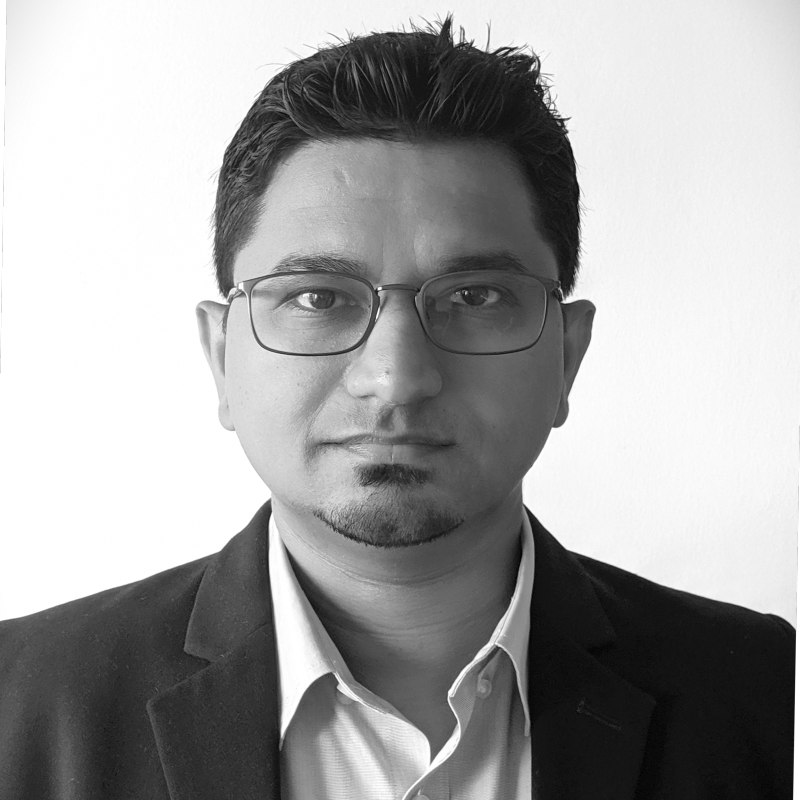 Black and white portrait of a man with glasses, short dark hair, wearing a suit jacket and collared shirt against a plain background.