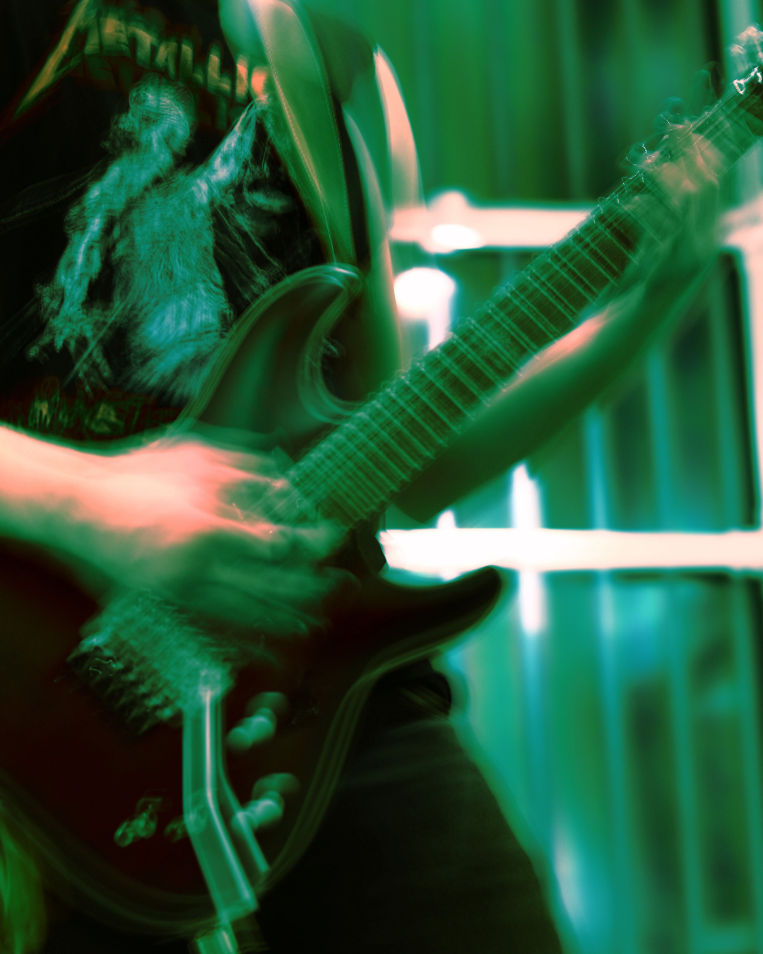 Close-up of a person playing an electric guitar with a blurred, vibrant green and red lighting effect.