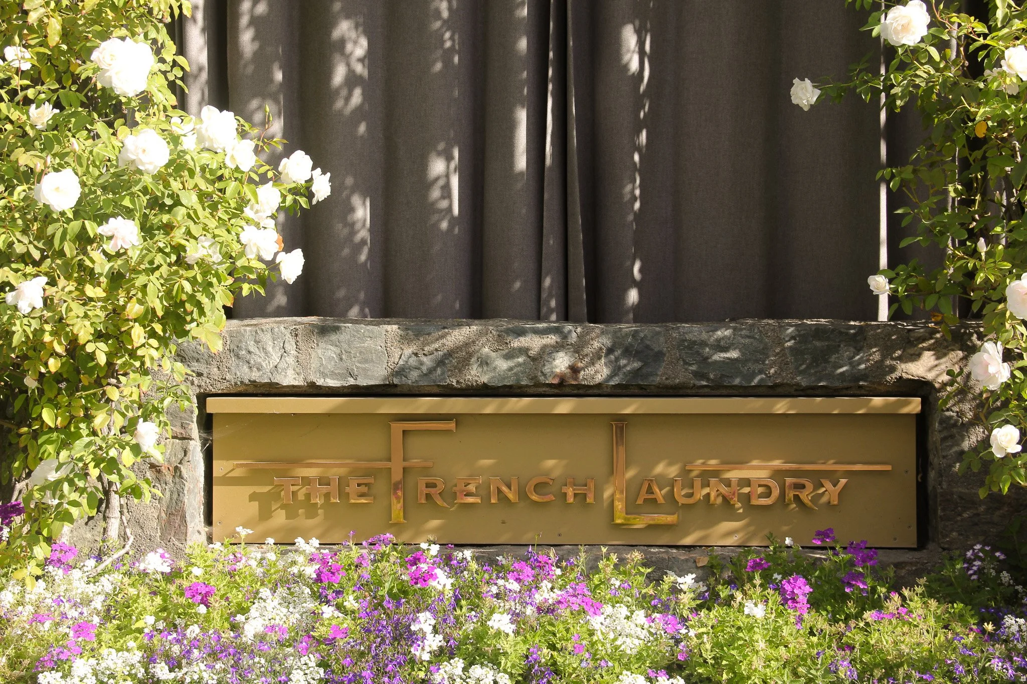 Sign for The French Laundry restaurant surrounded by blooming white and purple flowers and greenery.