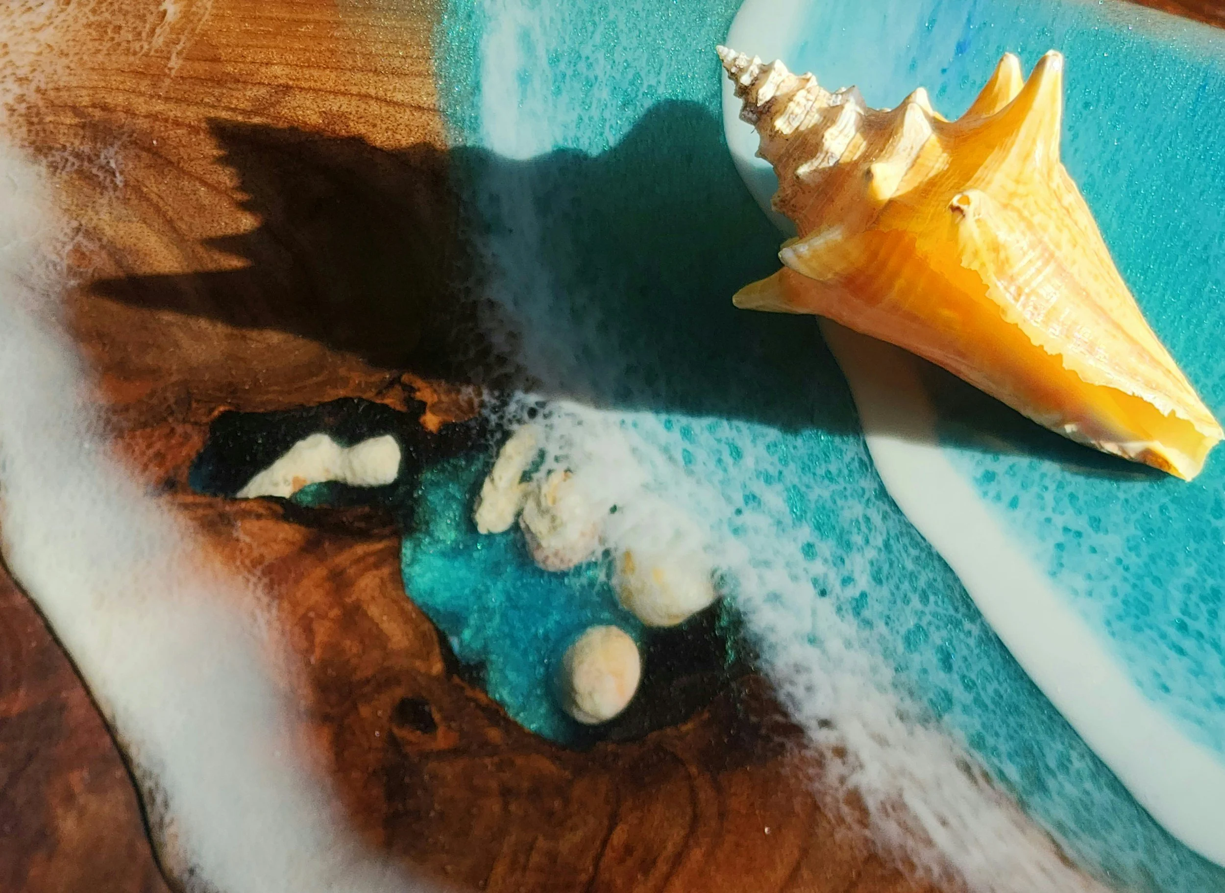 Close-up of a seashell on an ocean blue resin background with some white sea foam lining the waves.
