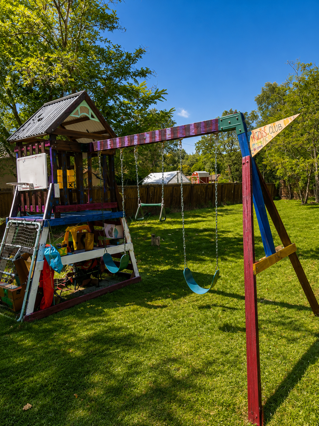 Colorful backyard playground with a swing set, slide, and climbing structure, surrounded by green grass and trees on a sunny day.