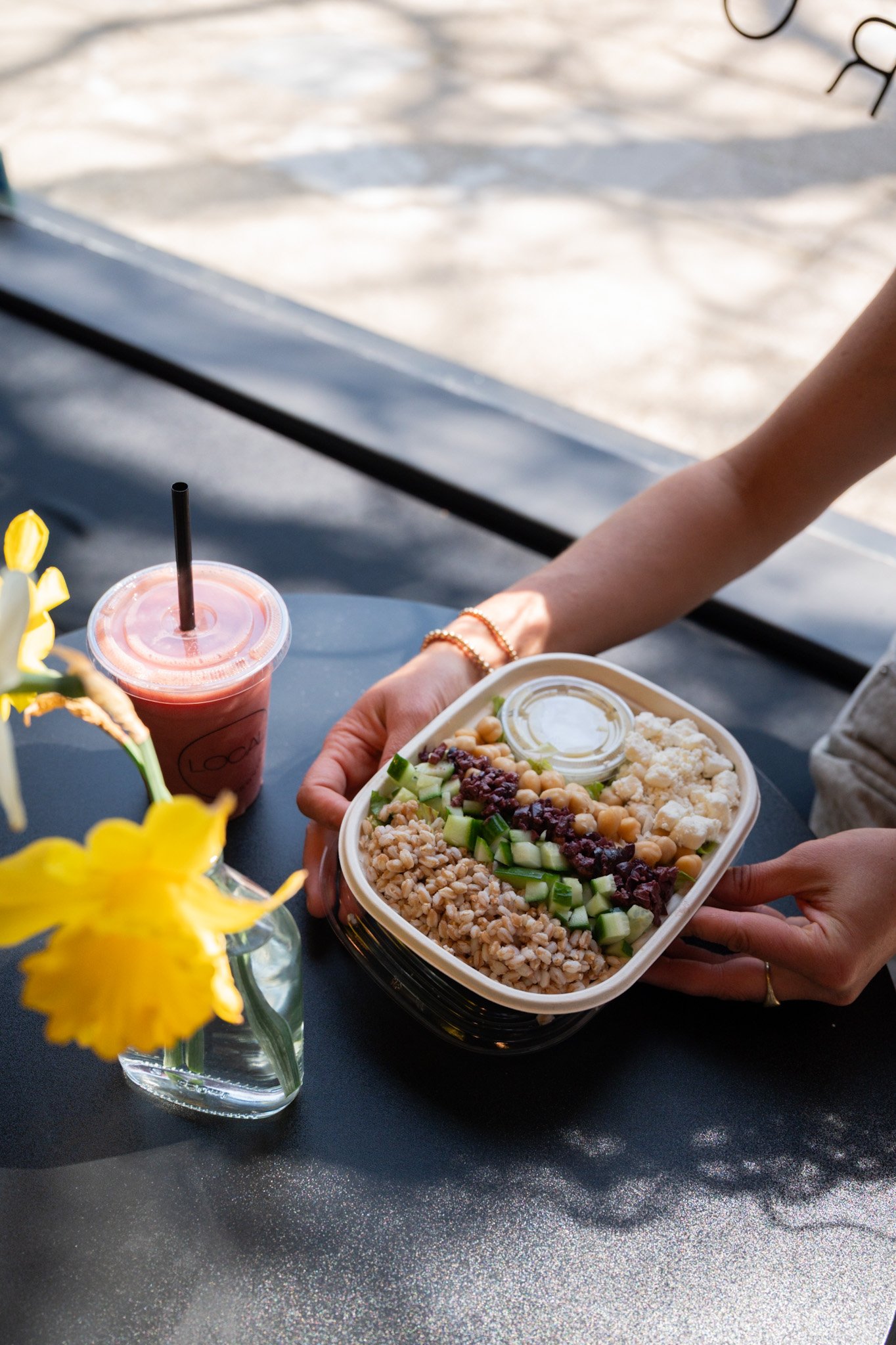 Healthy salad bowl with quinoa, shredded carrots, pumpkin seeds, feta cheese, diced apples, diced beets, and a cup of dressing, held by a person in a white sweater.
