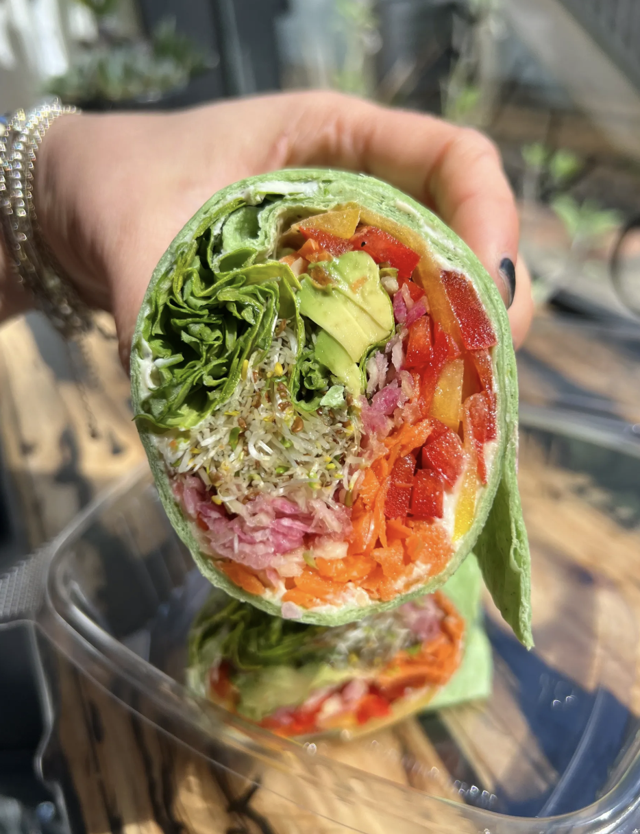 Close-up of a fresh vegetable wrap filled with greens, avocado, rice, shredded ham, and chopped red and yellow bell peppers.