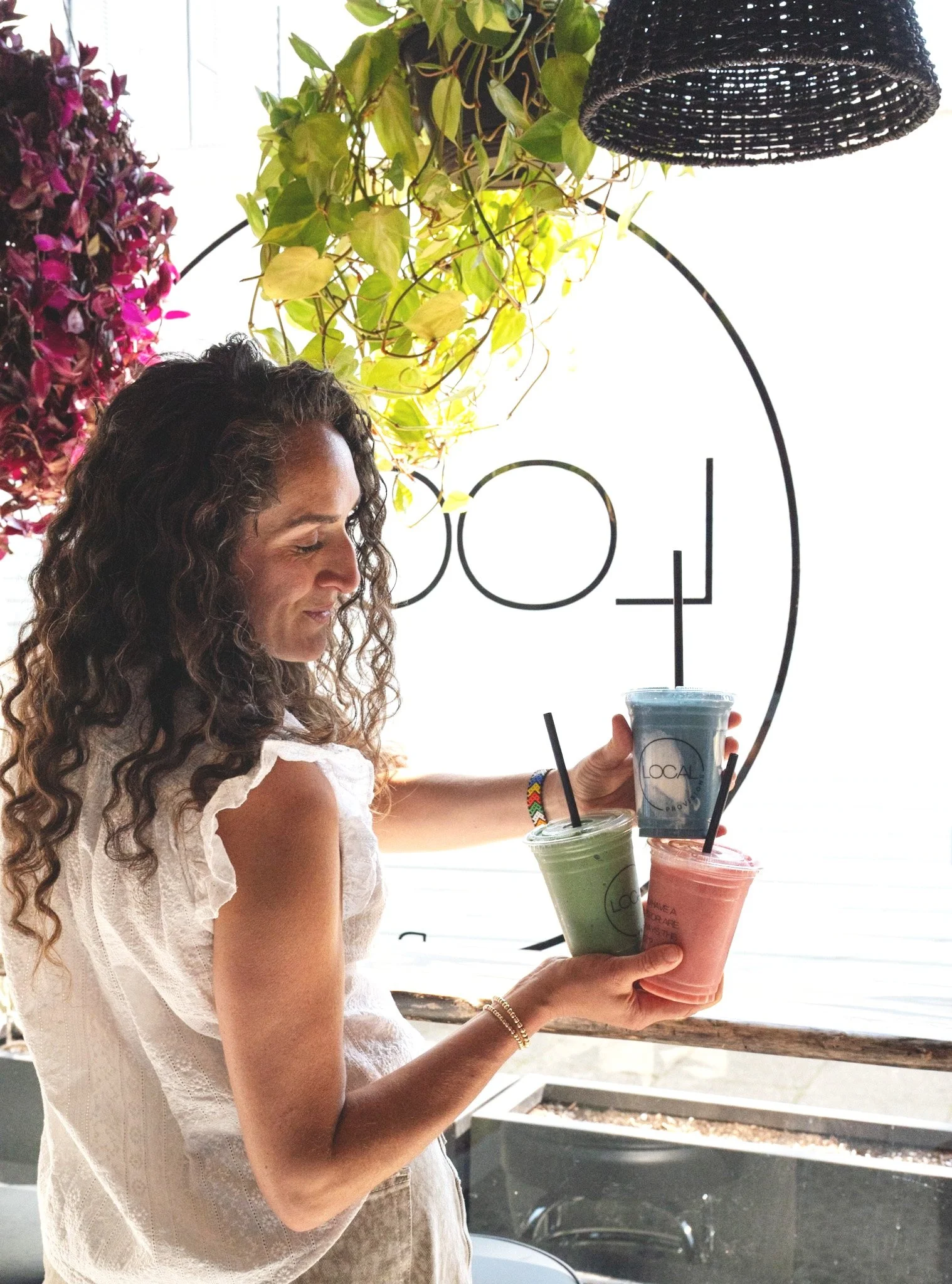 Hand holding a purple smoothie in a clear plastic cup with green plants in the background. The cup features the text "IF YOU WERE A FRUIT YOU'D BE A FINEAPPLE #LOCALL♥VE."