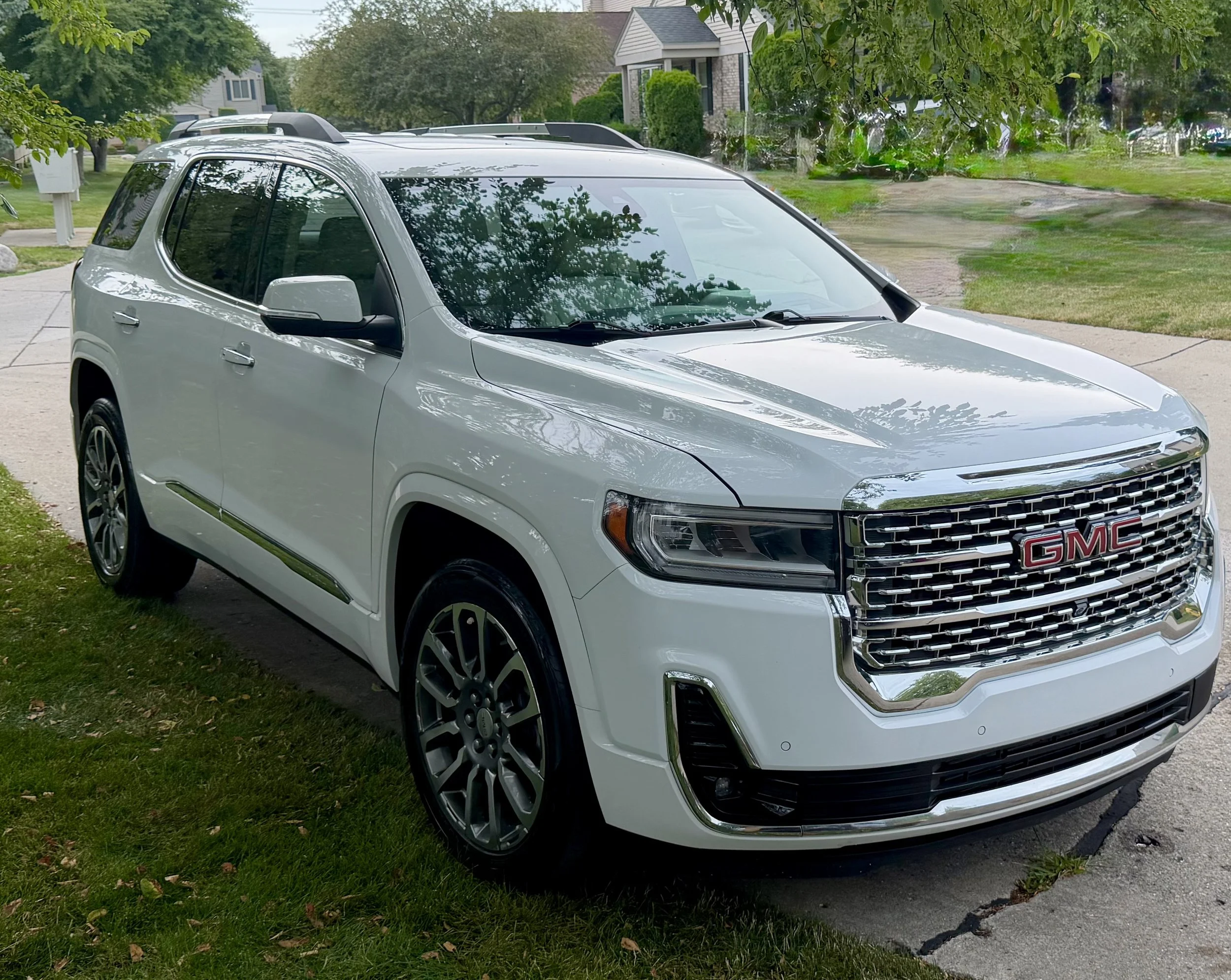A silver GMC SUV parked on the driveway of a residential neighborhood, with trees and houses in the background.