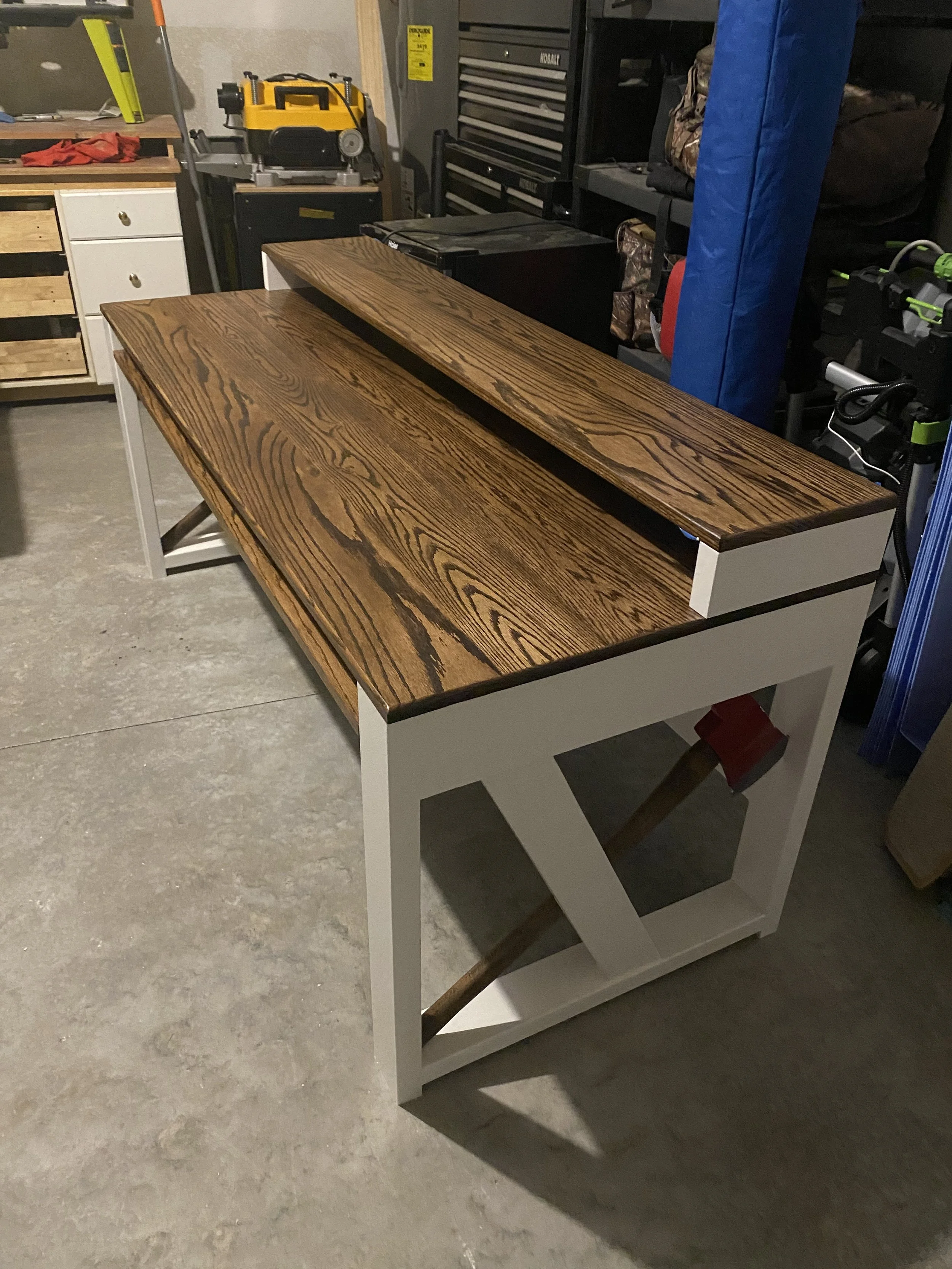 A wooden table with a white base in a workshop or garage, surrounded by various tools, storage cabinets, and equipment.