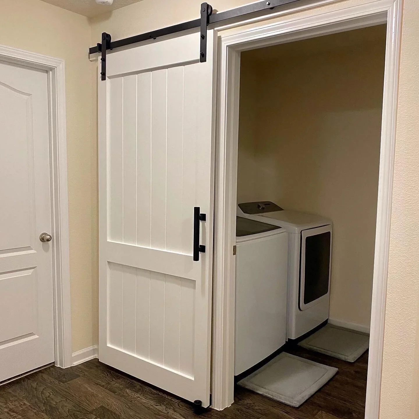Bathroom with a sliding barn door leading to a small laundry area with a washing machine, a dryer, and a small rug on a wood floor.