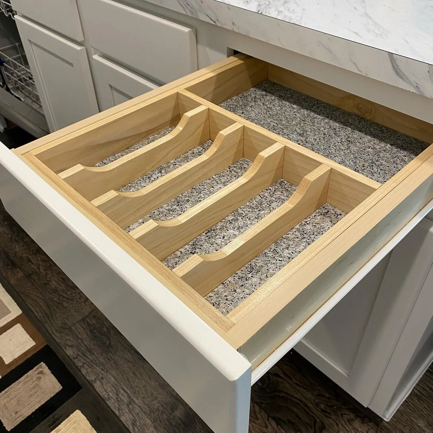 Open kitchen drawer with wooden storage organizer, multiple compartments, and granite countertop.