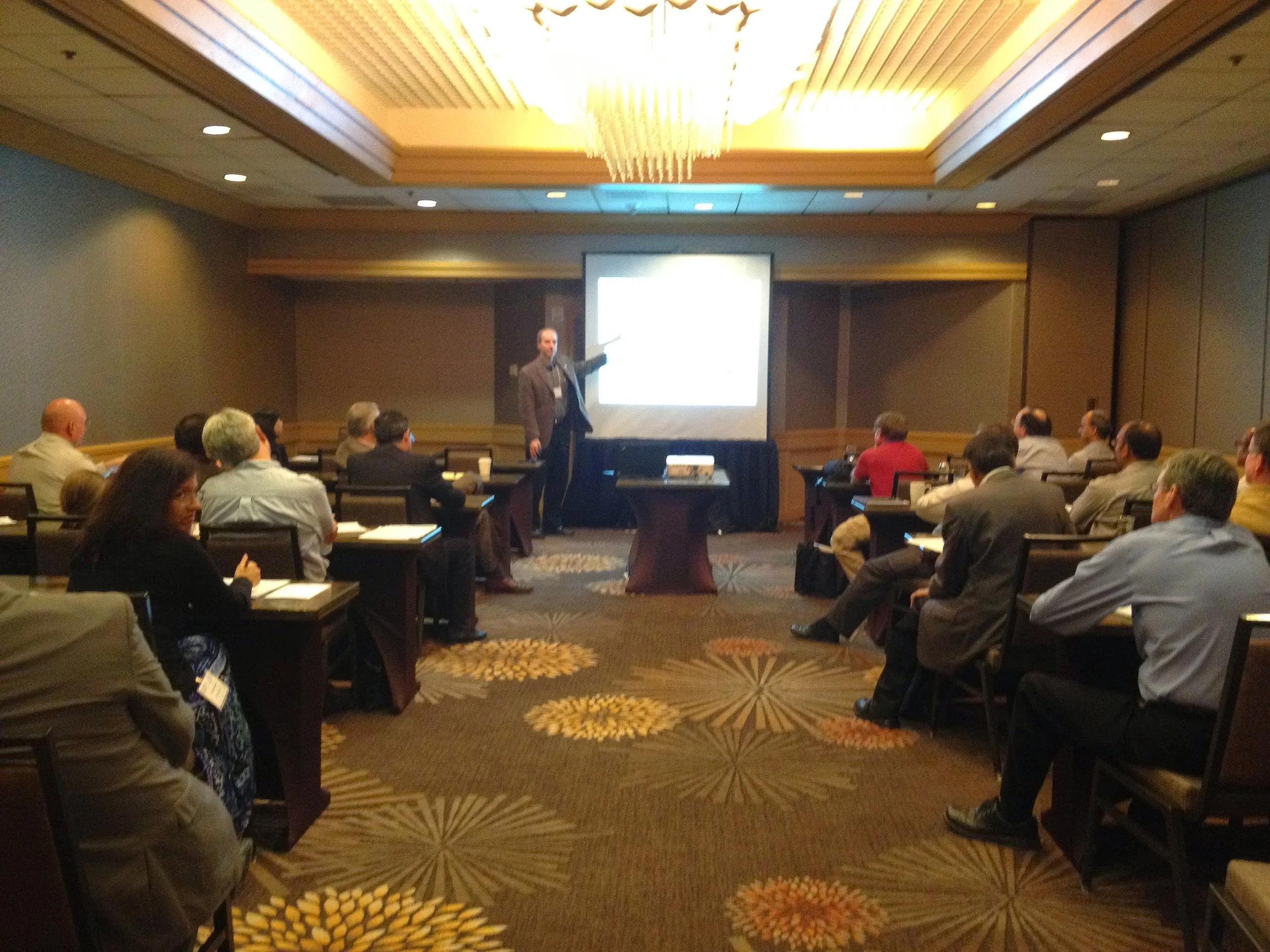 Barclay R. Brown at a conference giving a presentation to an audience seated in a dimly lit banquet room.