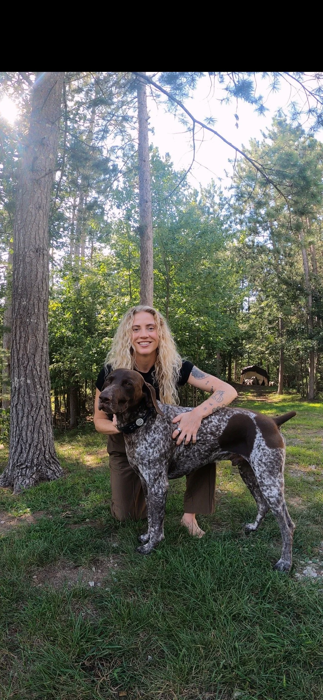 Dr. Paige Weyer smiling with her dog in a peaceful wooded setting, reflecting her connection to nature and holistic health