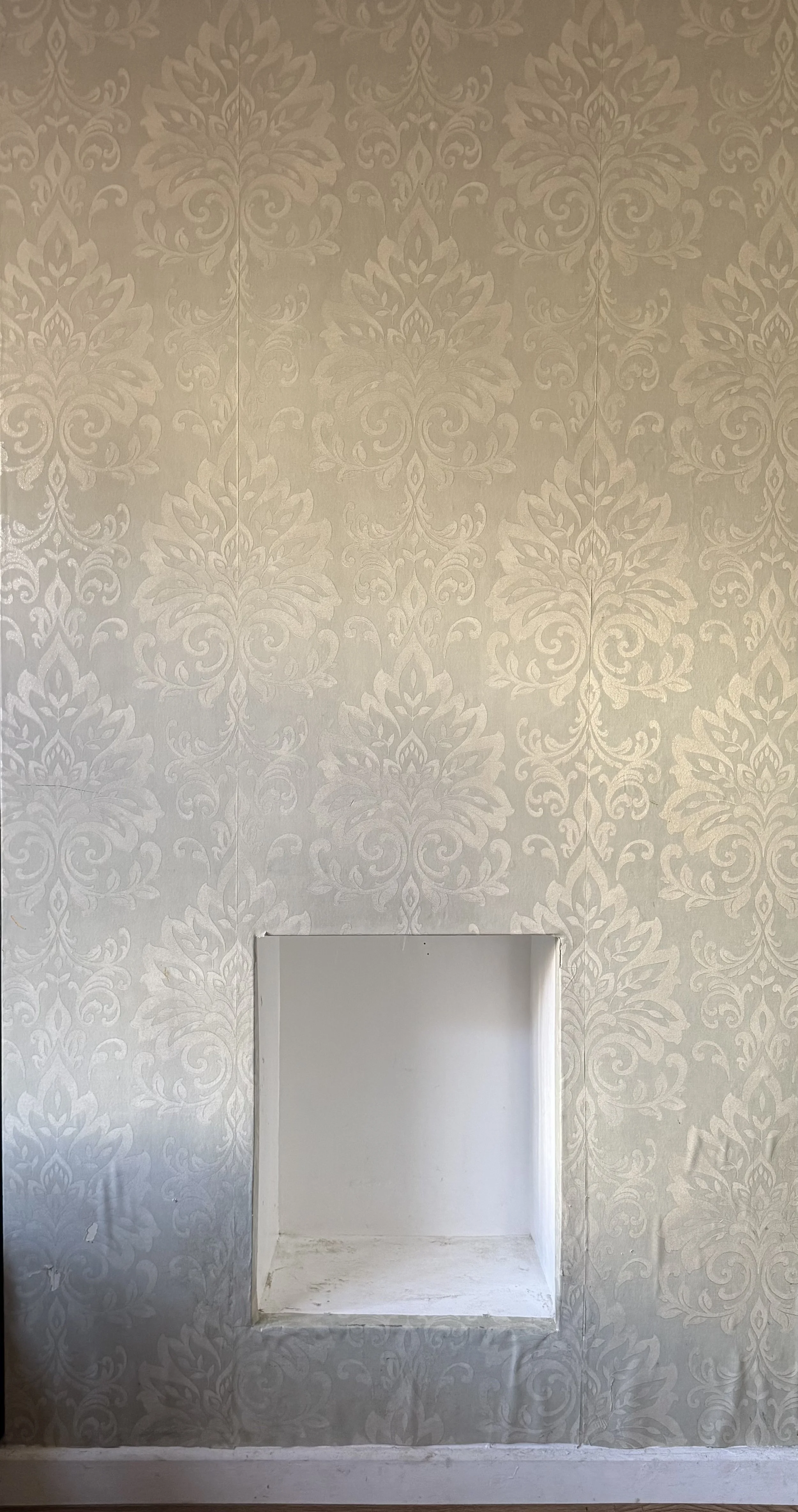 A wall with beige damask-patterned wallpaper and a rectangular opening or alcove.