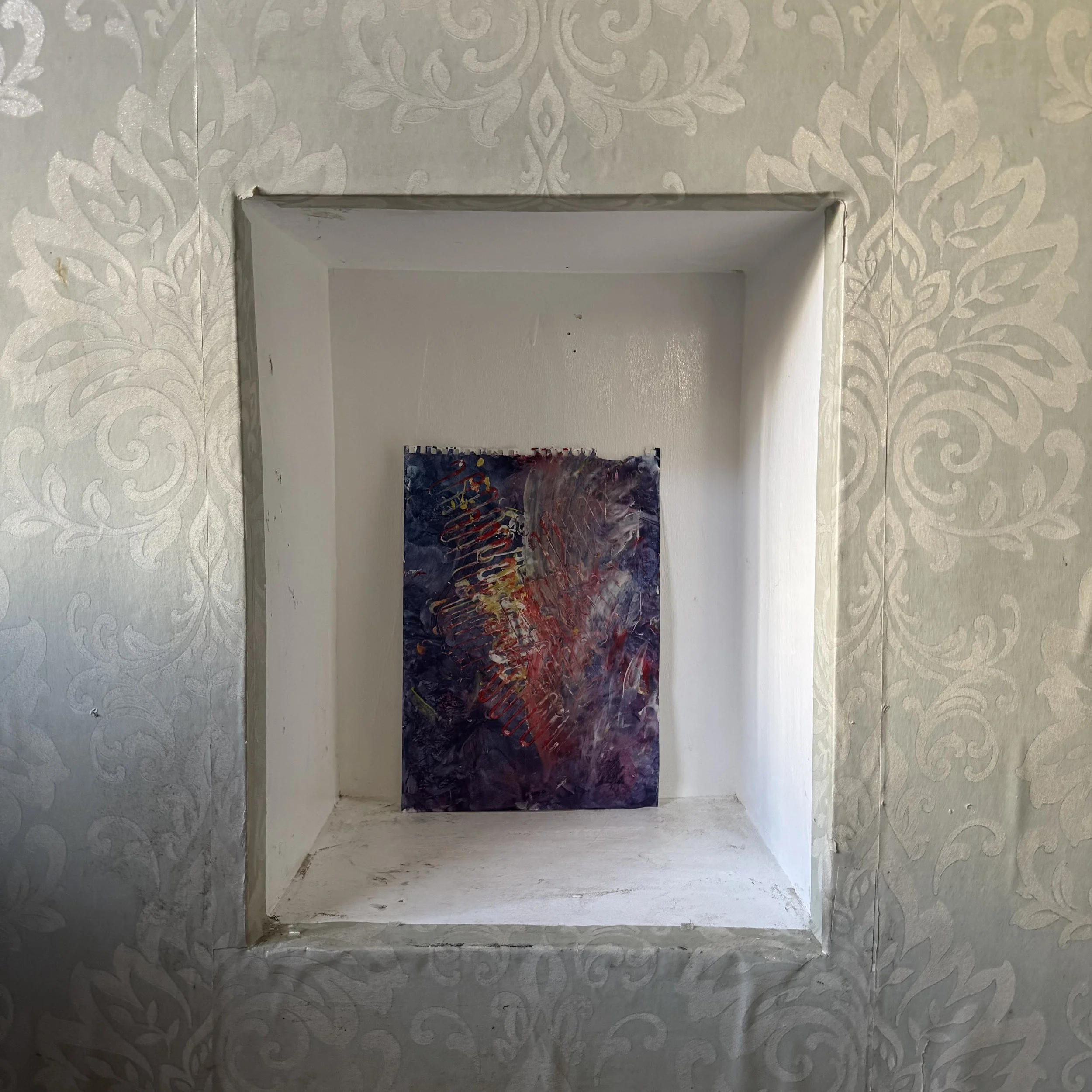 A painted modern abstract artwork with blue, red, yellow, and white colors situated on a white wall within a recessed wall niche. The niche is surrounded by a white textured wallpaper with a floral pattern by Evie Sofia Forrest Norton (EVSN) at age 1