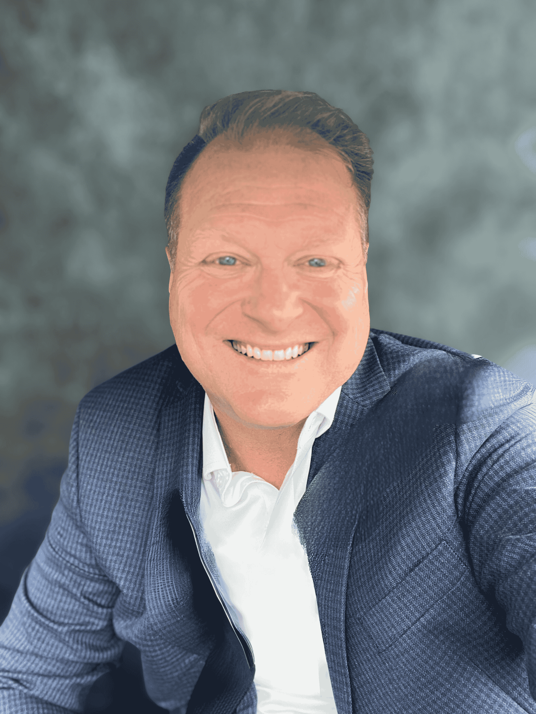 A smiling man with blue eyes, wearing a suit jacket over a white shirt, slightly leaning forward, with a gray textured background.