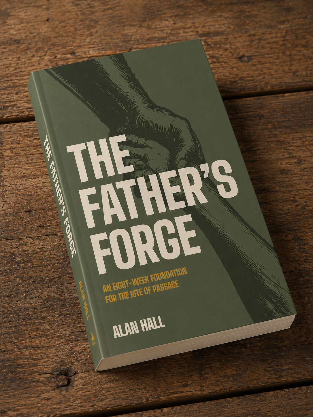A book titled 'The Father's Forge' by Alan Hall with a green cover, featuring an illustration of a hand from above of a father, reaching down and grasping the hand of a son, resting on a wooden surface.
