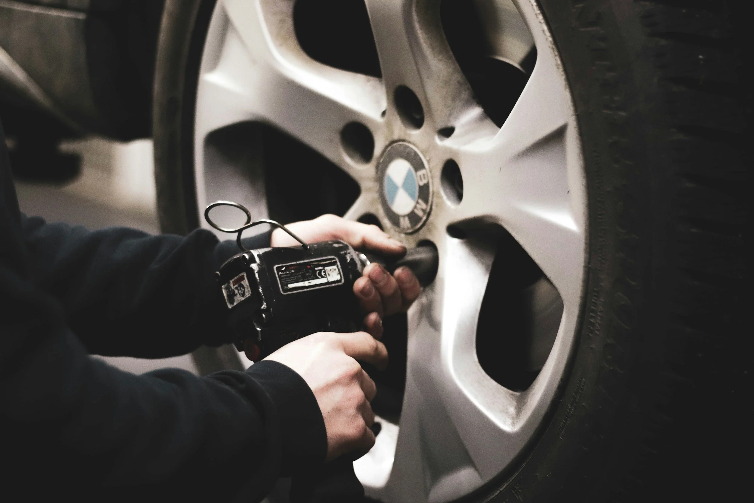 Person using an electric drill to tighten or loosen a bolt on a car's wheel.
