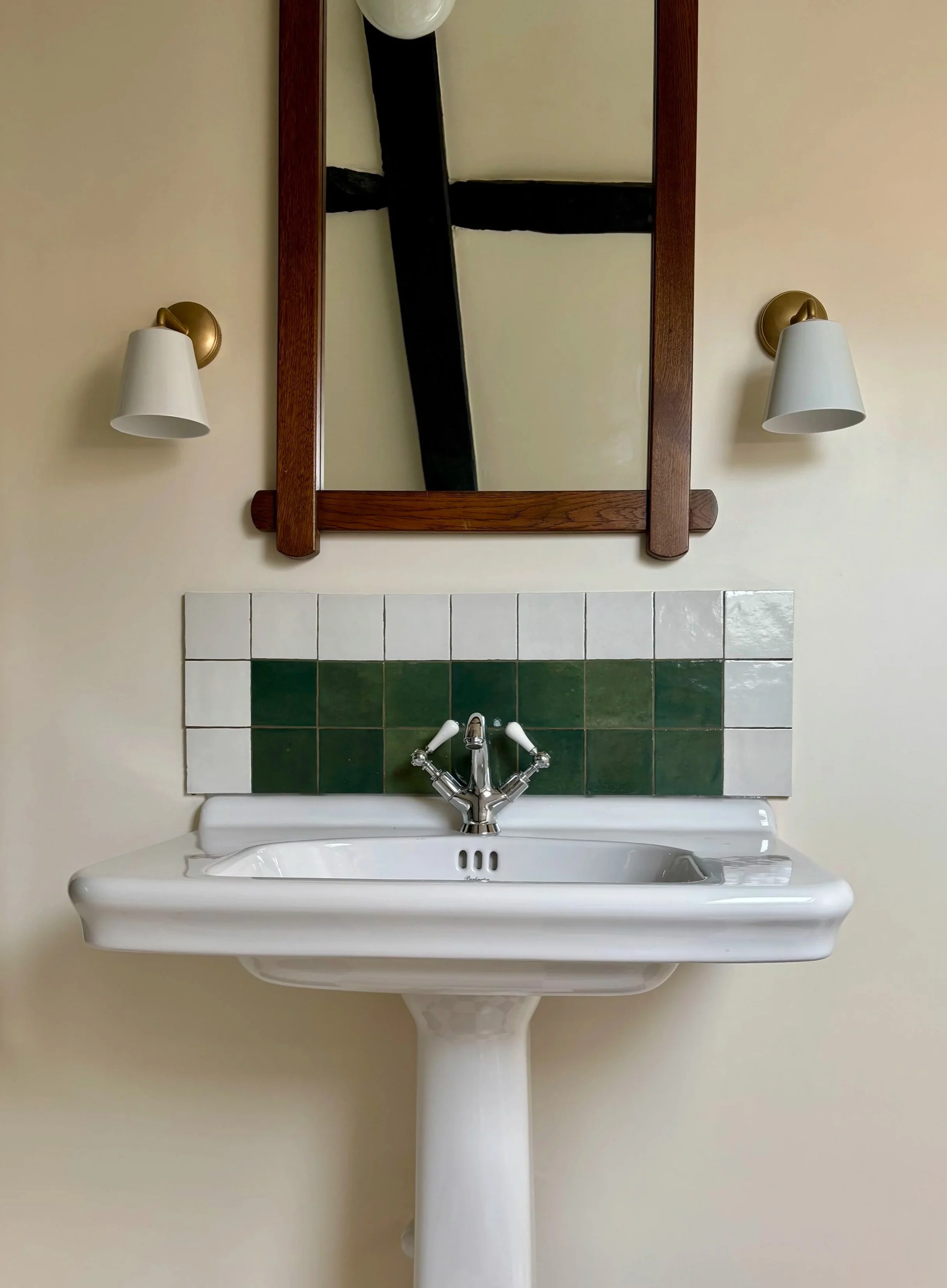 bathroom with limestone chequerboard floors, a sink with a green and white cplashback.  Wall lights with vintage brutalist mirror 