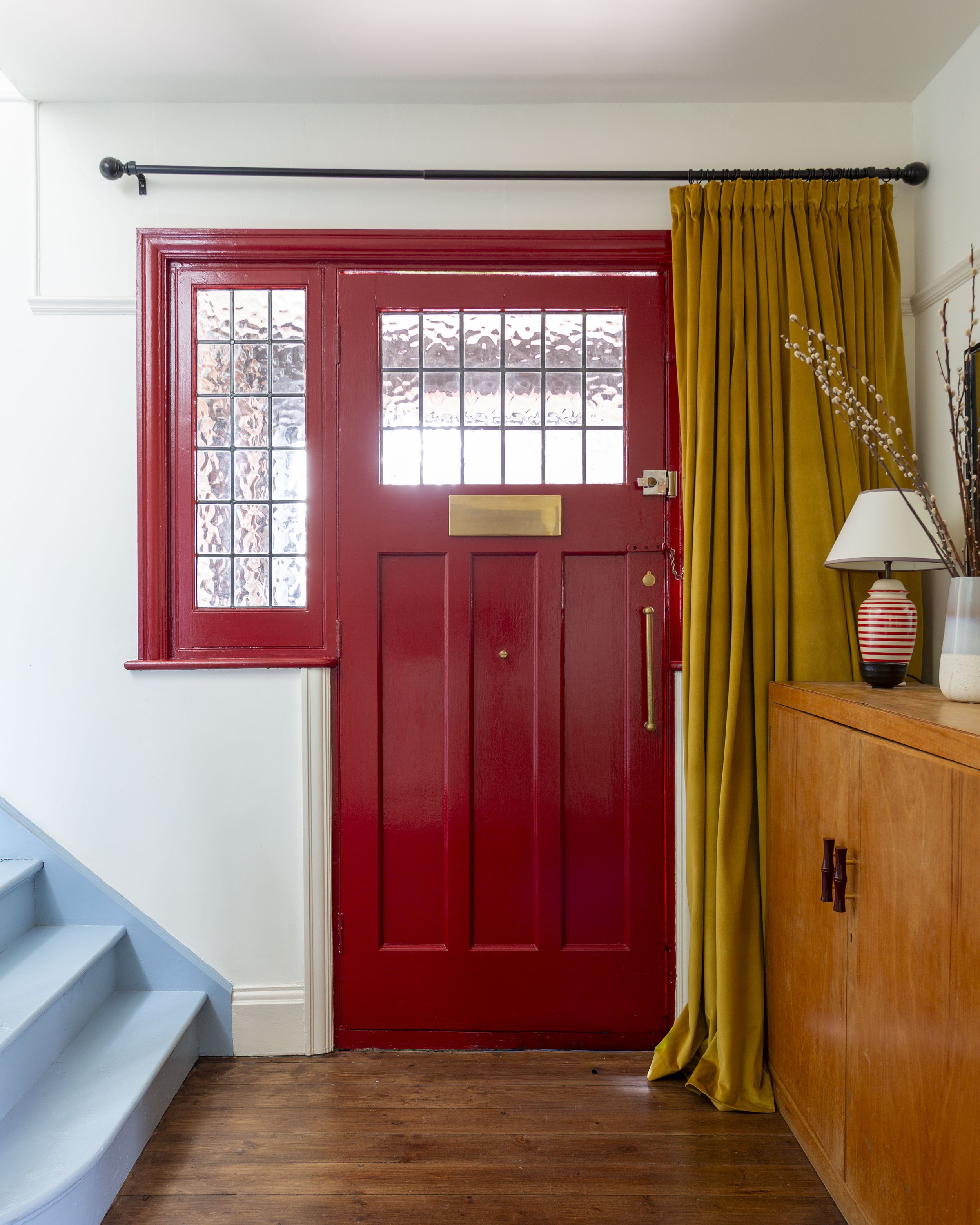 Red front door with yellow curtain and blue stairs