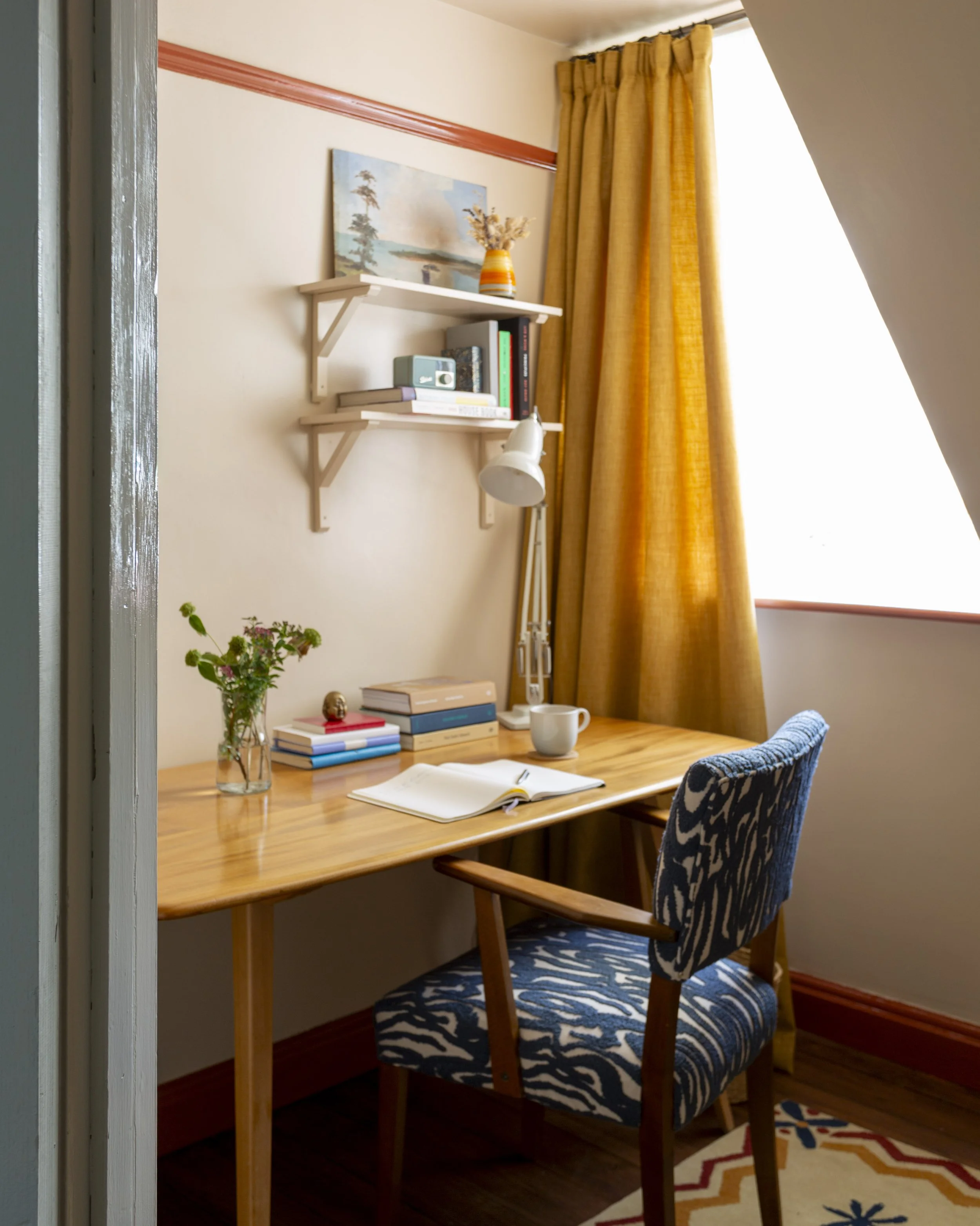 Study with soft pink walls and red woodwork. Yellow curtains and a blue patterned chair
