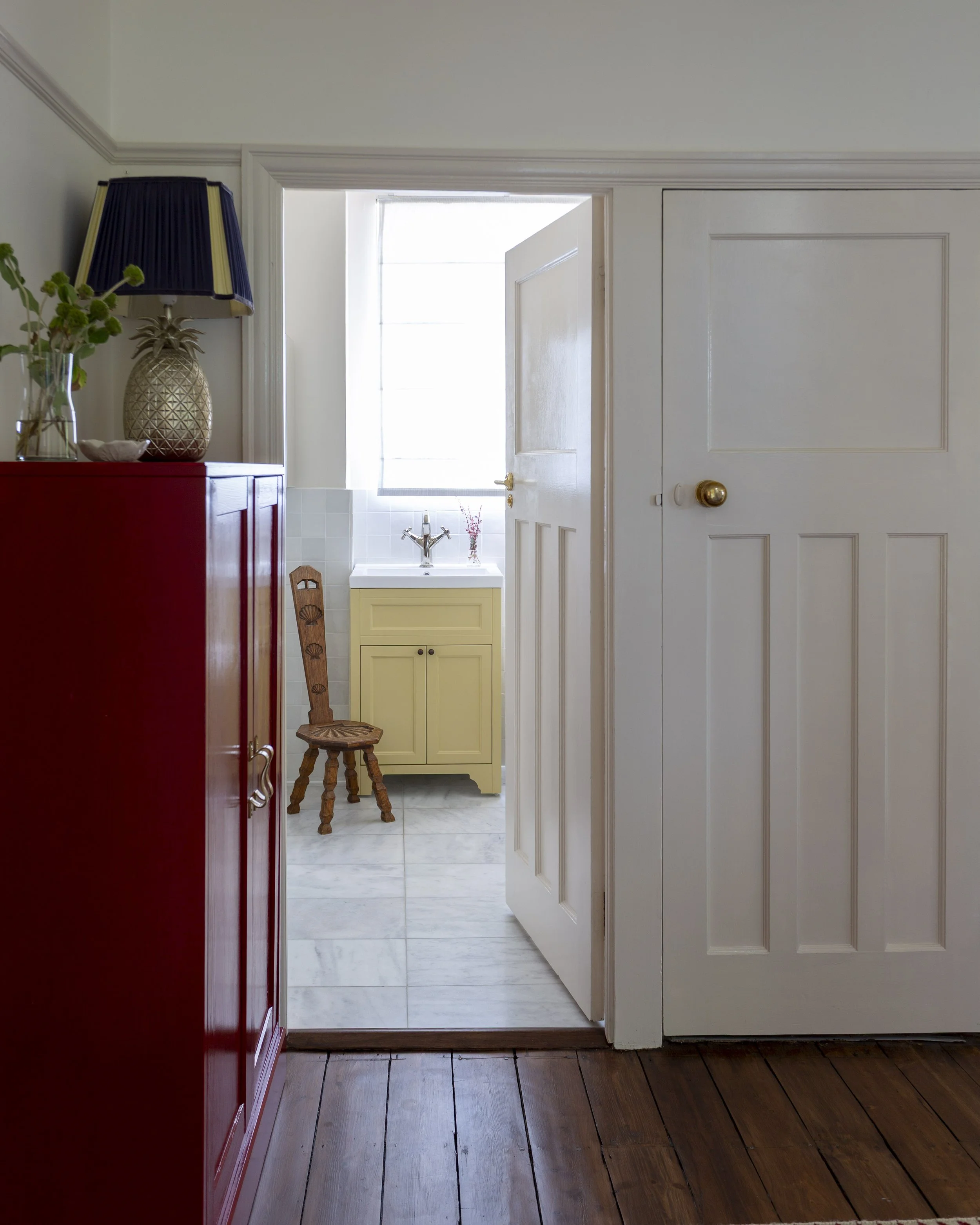 view from landing through to bathroom with yellow vanity unit and neutral tiles. red storage cupboard with lamp