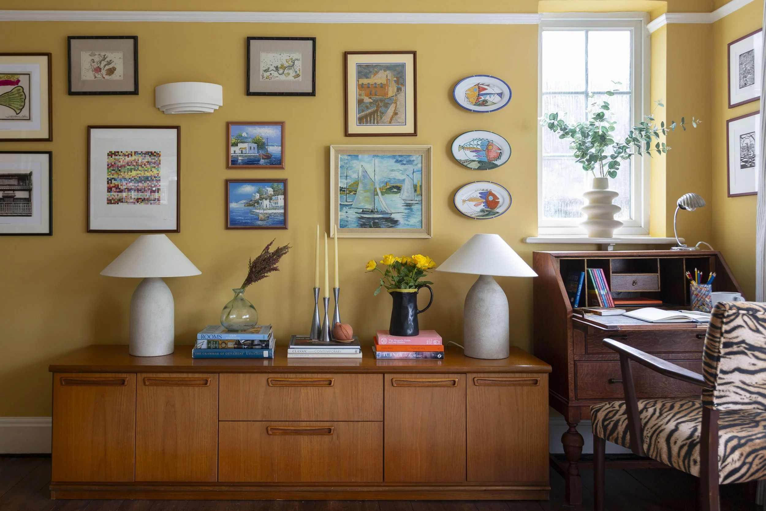 yellow living room with gallery wall, mid century sideboard, bureau desk and tiger print chair