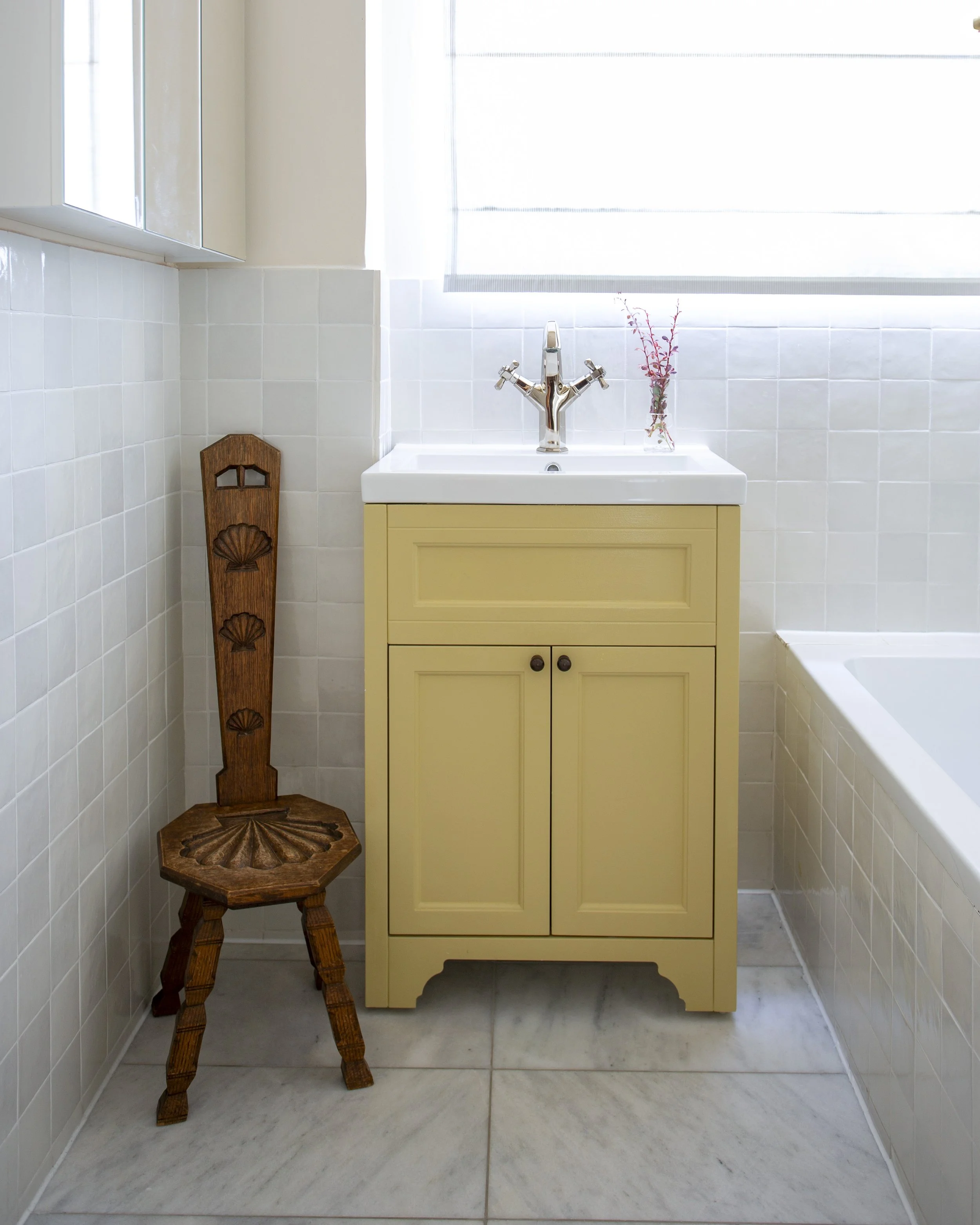 bathroom with white zellige tiles, marble floors and a yellow vanity. vintage shell seat
