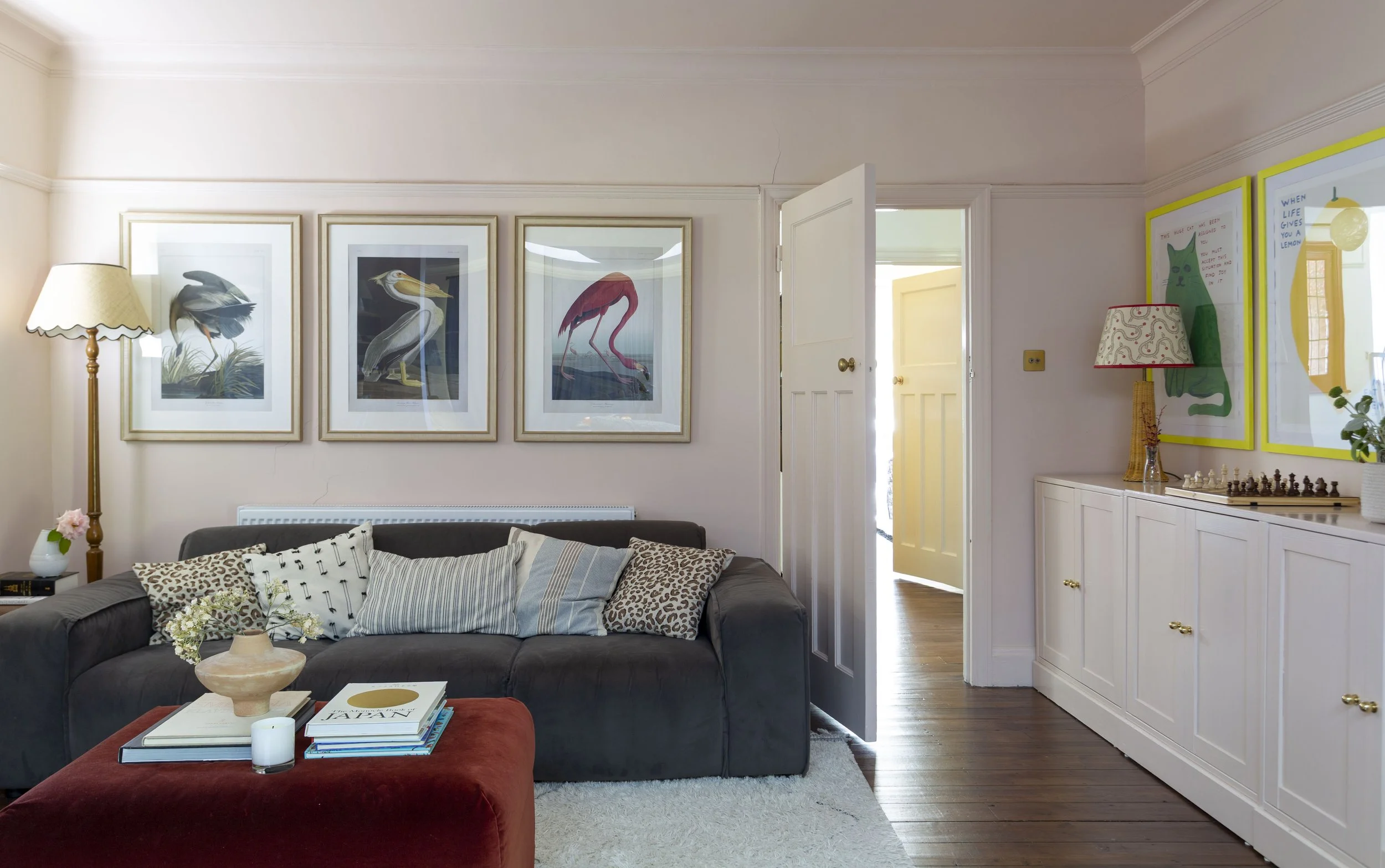 living room with grey sofa, red ottoman and soft pink walls 