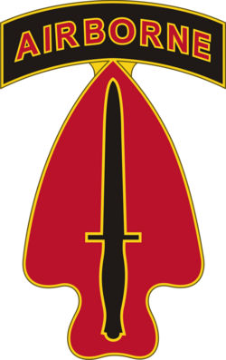 Military patch with a red arrowhead shape, black outline, and a black dagger in the center, topped with a black banner reading 'AIRBORNE' in yellow and red.
