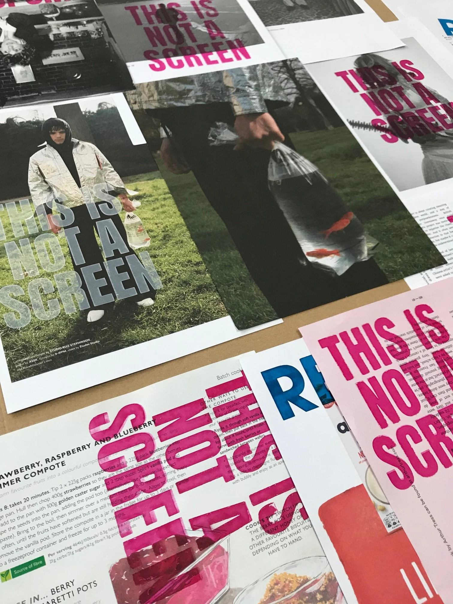 Printed pages with bold pink and blue text stating "This is not a screen" and other text, along with images of people and food items in a magazine or flyer layout.