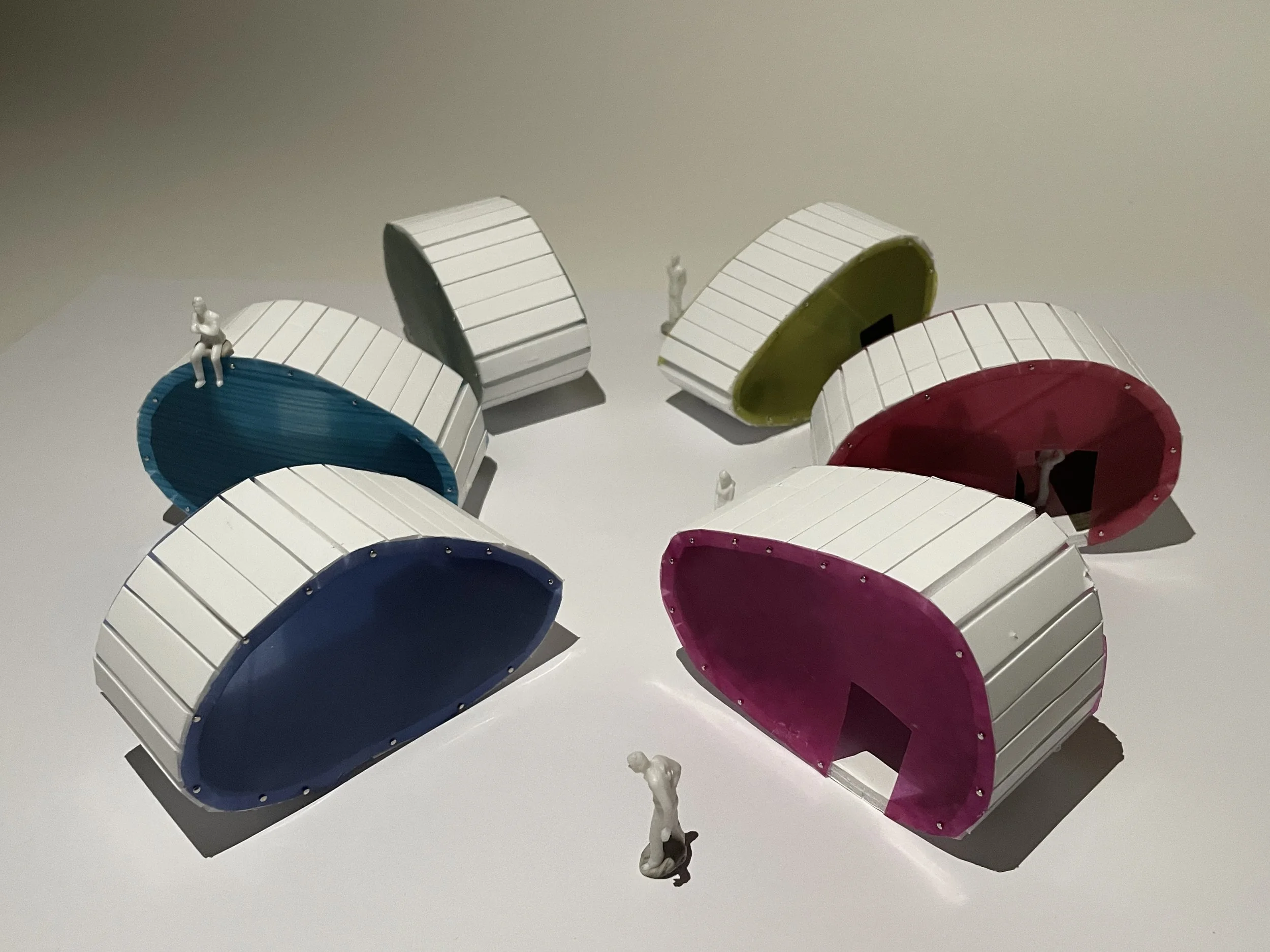 Colorful modern sculptures with small human figures are displayed against a plain background.