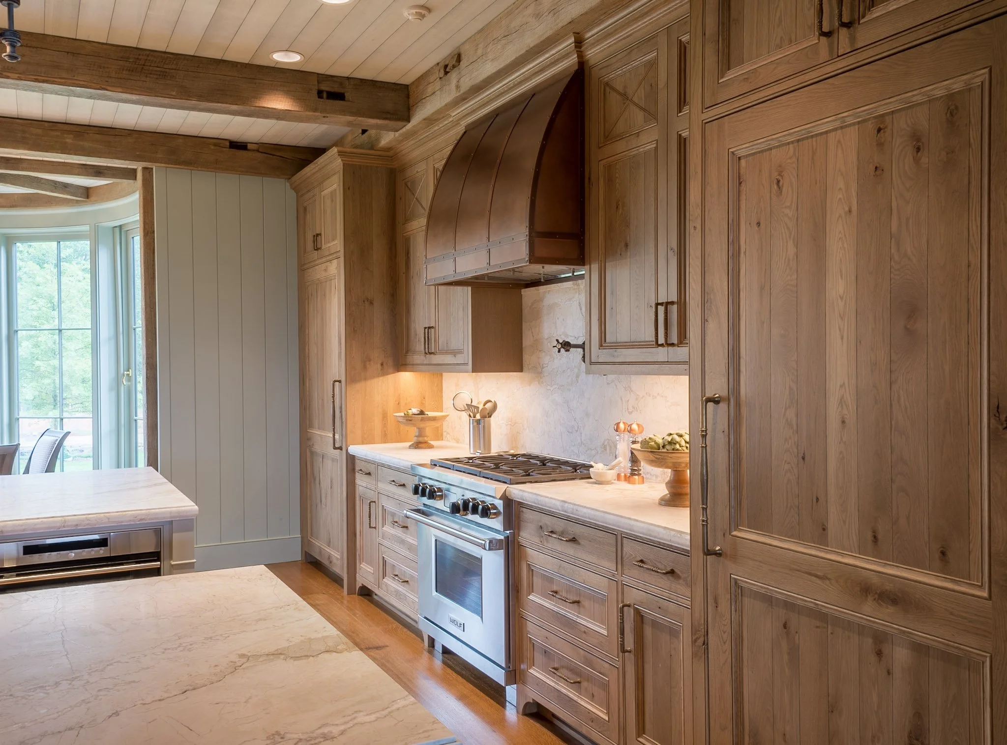 Kitchen with wooden cabinets, a stainless steel stove, a marble countertop, and a window with a view of green trees outside.