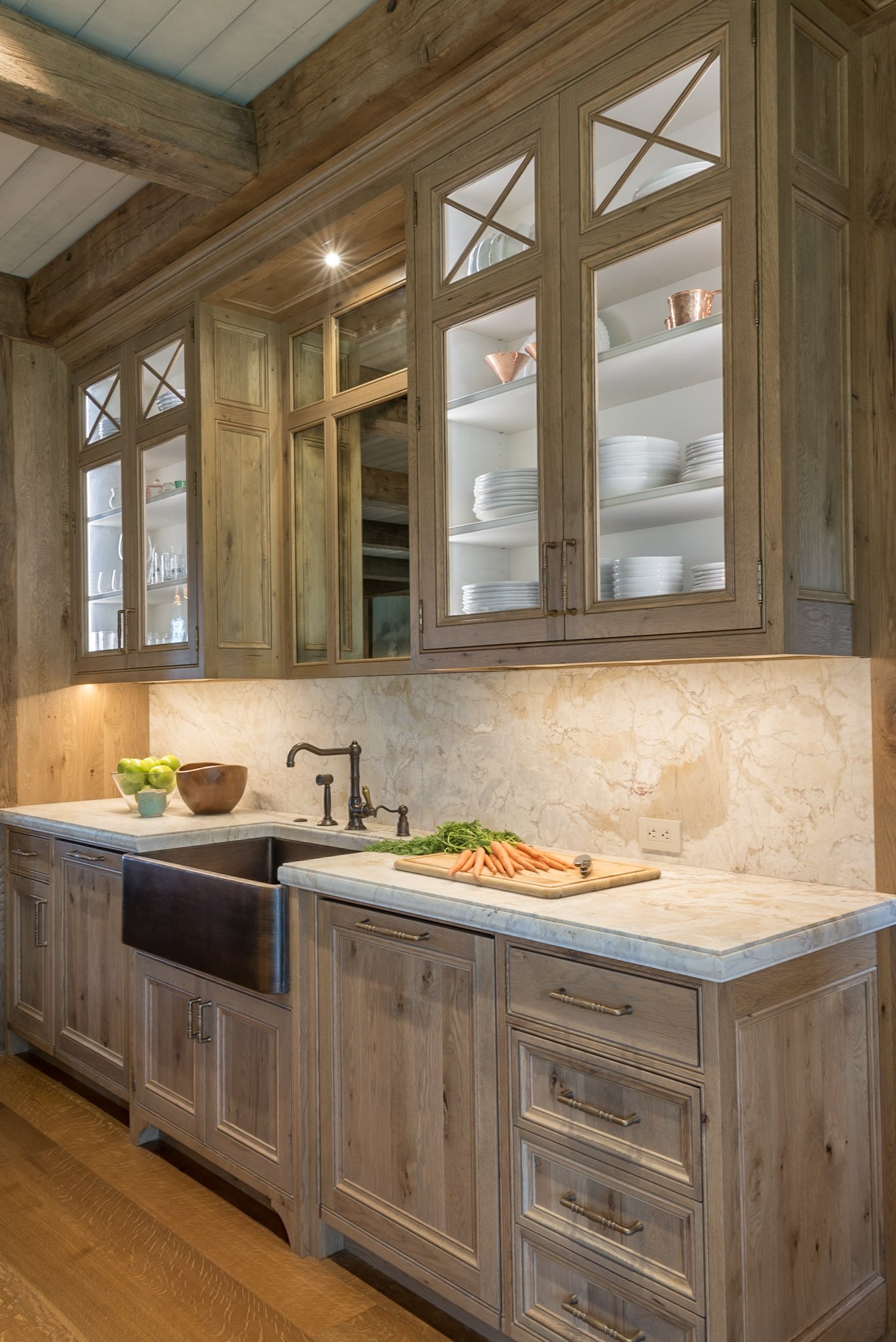 Kitchen with wooden cabinetry, open shelving, a marble countertop, a farmhouse sink, and carrots on a cutting board.
