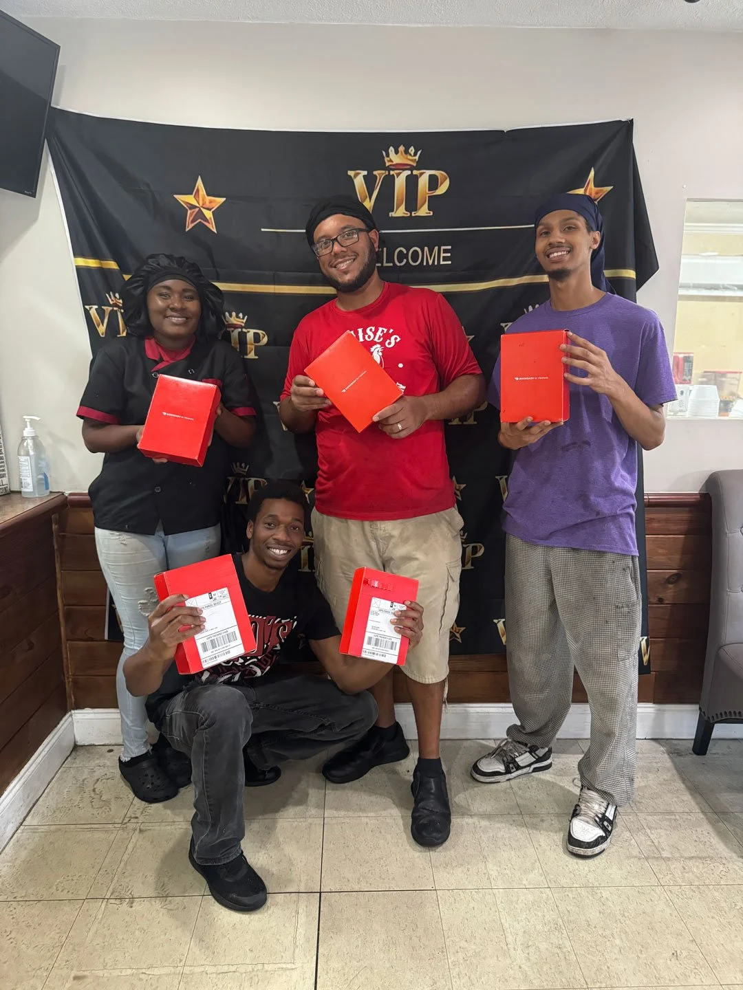 Group of five people celebrating with red boxes in front of a VIP banner at a restaurant or cafe.