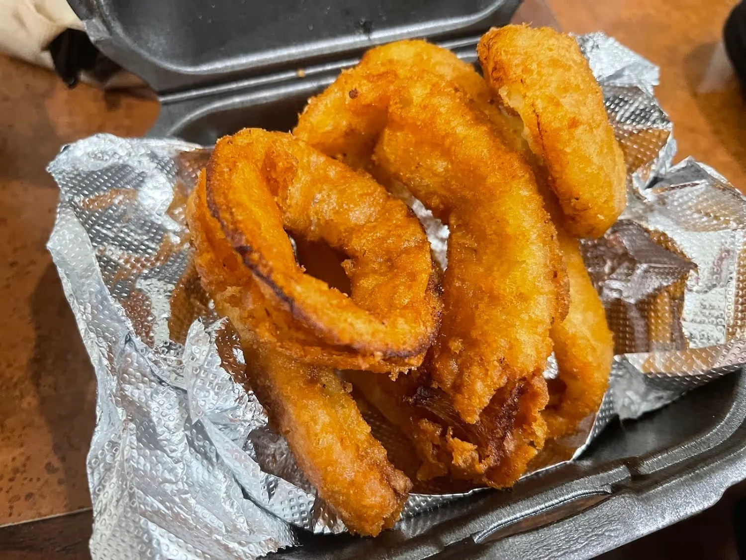Fried onion rings on a bed of foil in a plastic basket.