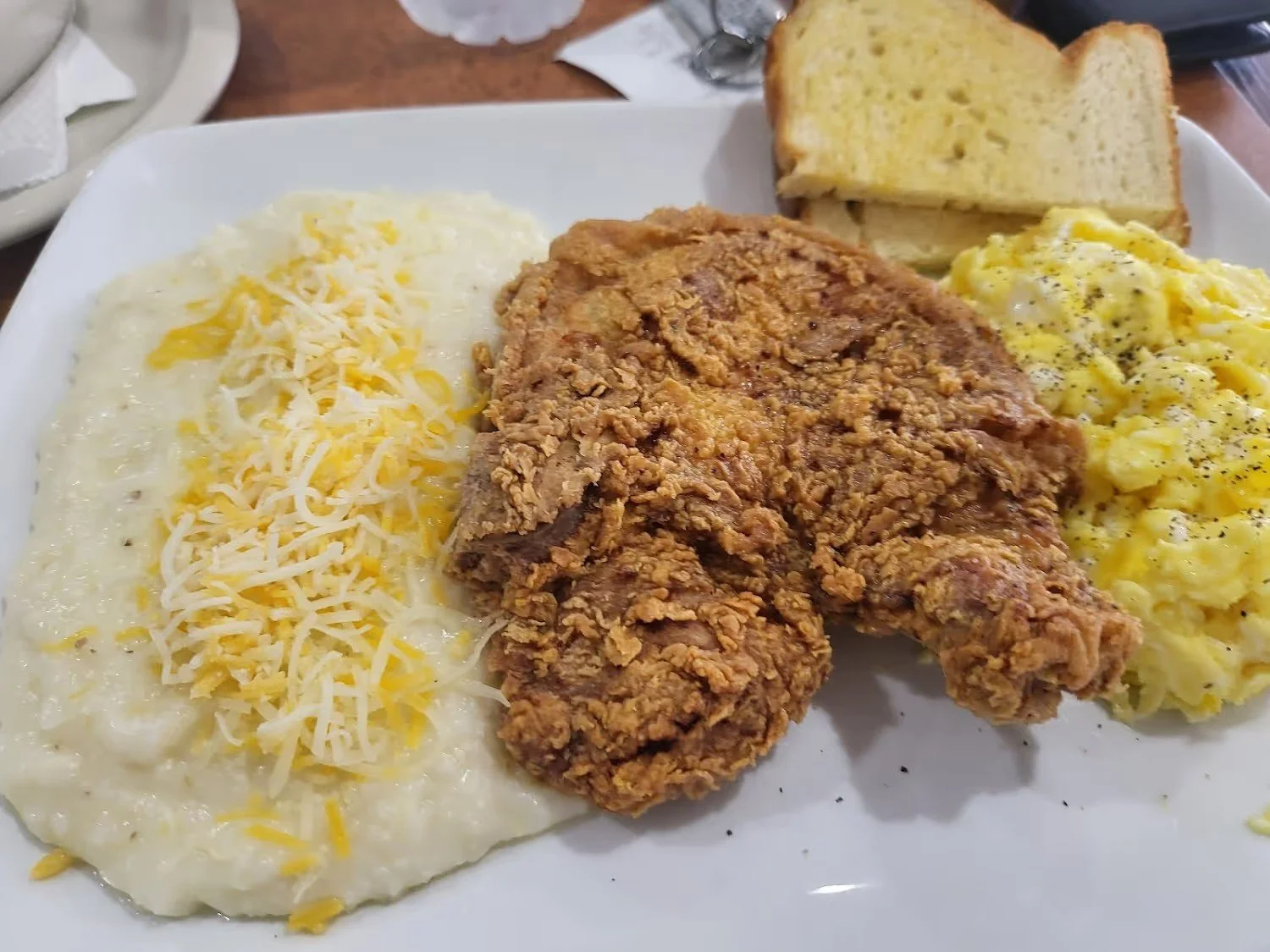 Plate of food with cheesy mashed potatoes, fried chicken leg, scrambled eggs, and slices of bread.