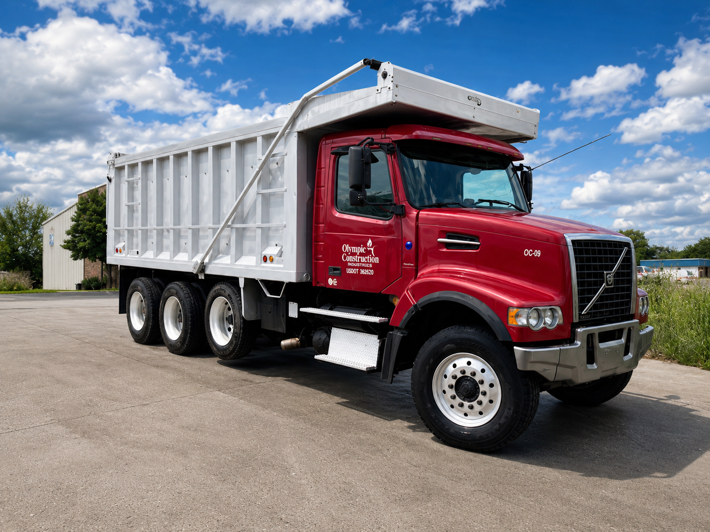 Red construction truck with a white dump bed, parked on a concrete surface under a partly cloudy sky.