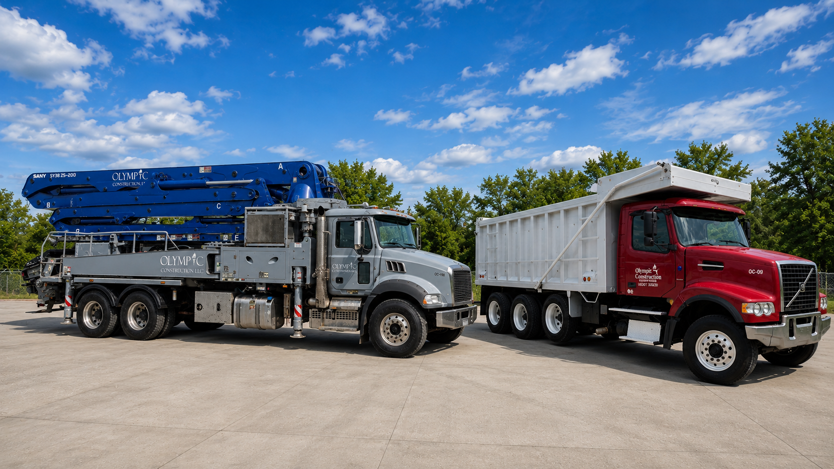 A construction truck with a blue crane parked next to a red dump truck on a concrete lot with green trees and a partly cloudy sky in the background.