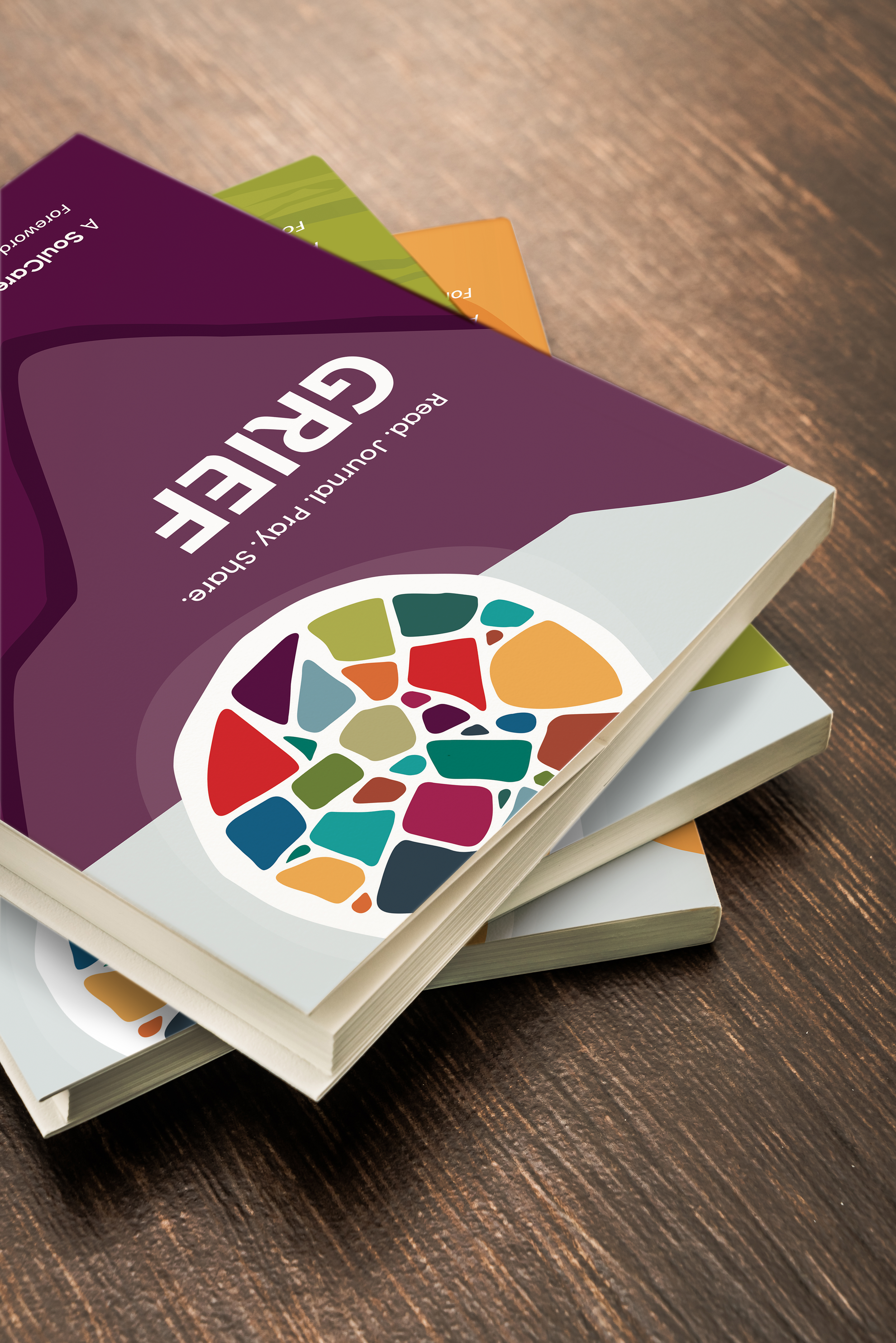 Close-up of three colorful books stacked on a wooden surface, with the top book titled 'The Guide' and featuring a multicolored circular graphic on the cover.