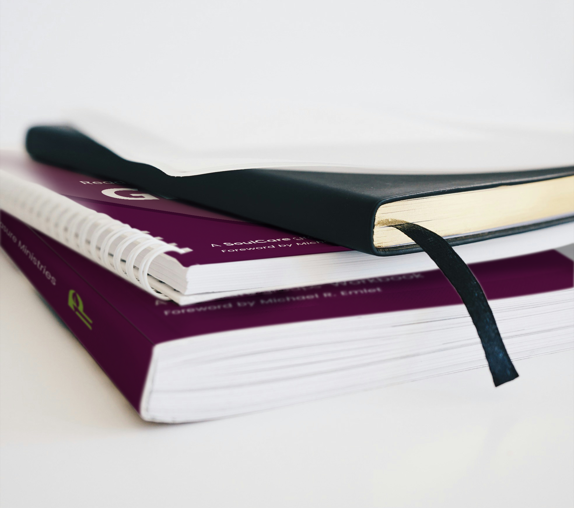 Close-up of stacked academic and medical textbooks, with a black notebook on top and a white spiral-bound notebook beneath, on a white surface.