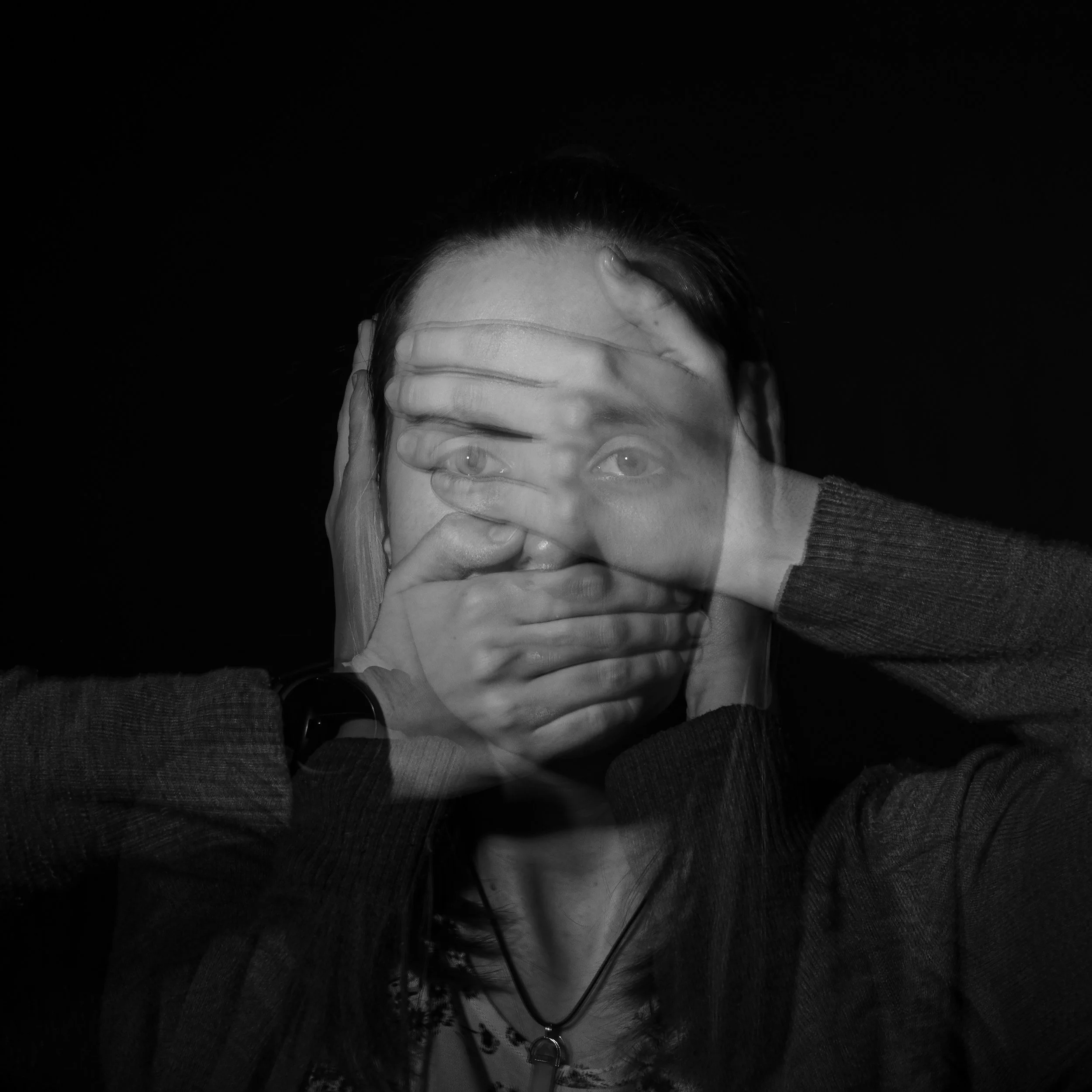 A black and white abstract photo of a person covering their mouth and their closed eyes with their hands while scrunching their face.