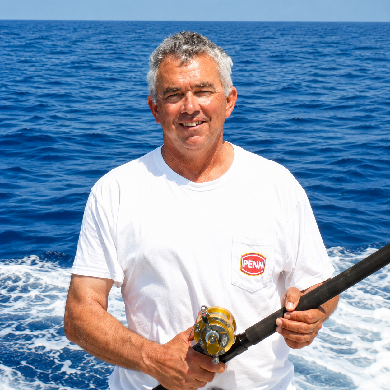 Smiling older man with gray hair fishing on a boat in the ocean, wearing a white t-shirt with a 'PENN' logo, holding a fishing rod.