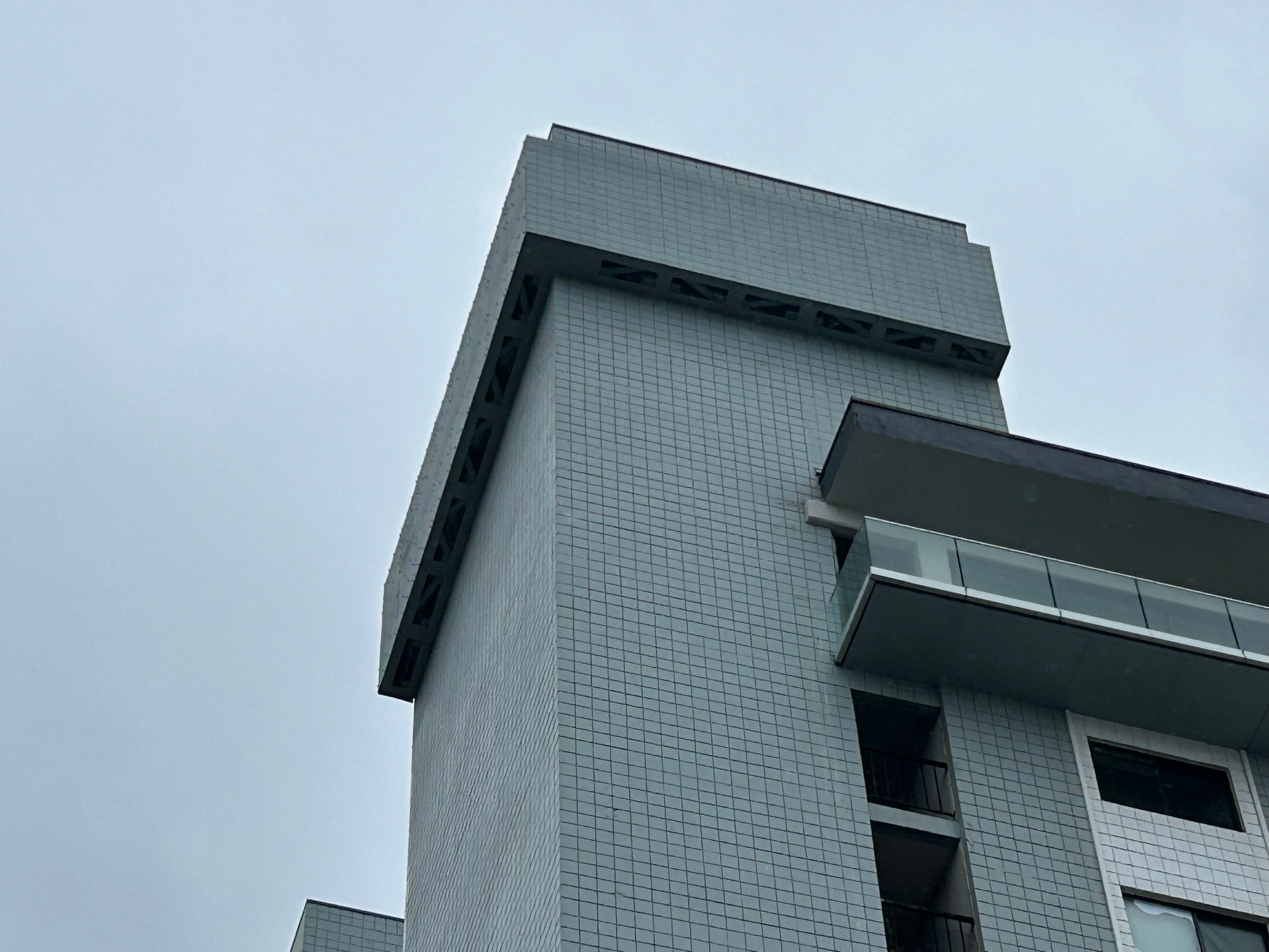 Low-angle view of a modern white building with a textured surface and balcony, against an overcast sky.