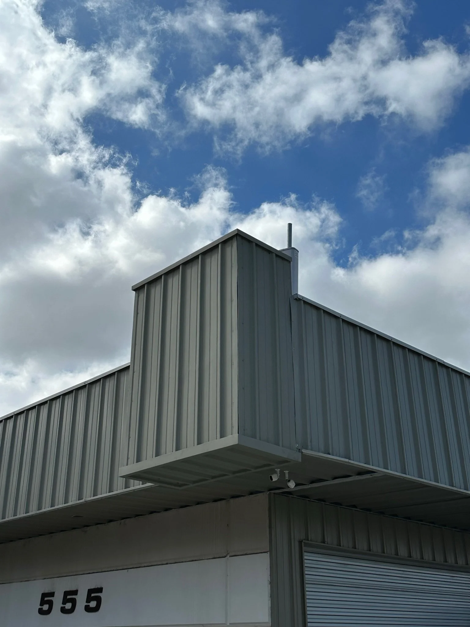 The corner of a modern industrial building with metal siding and a roll-up garage door, with the number 555 visible on the wall below.