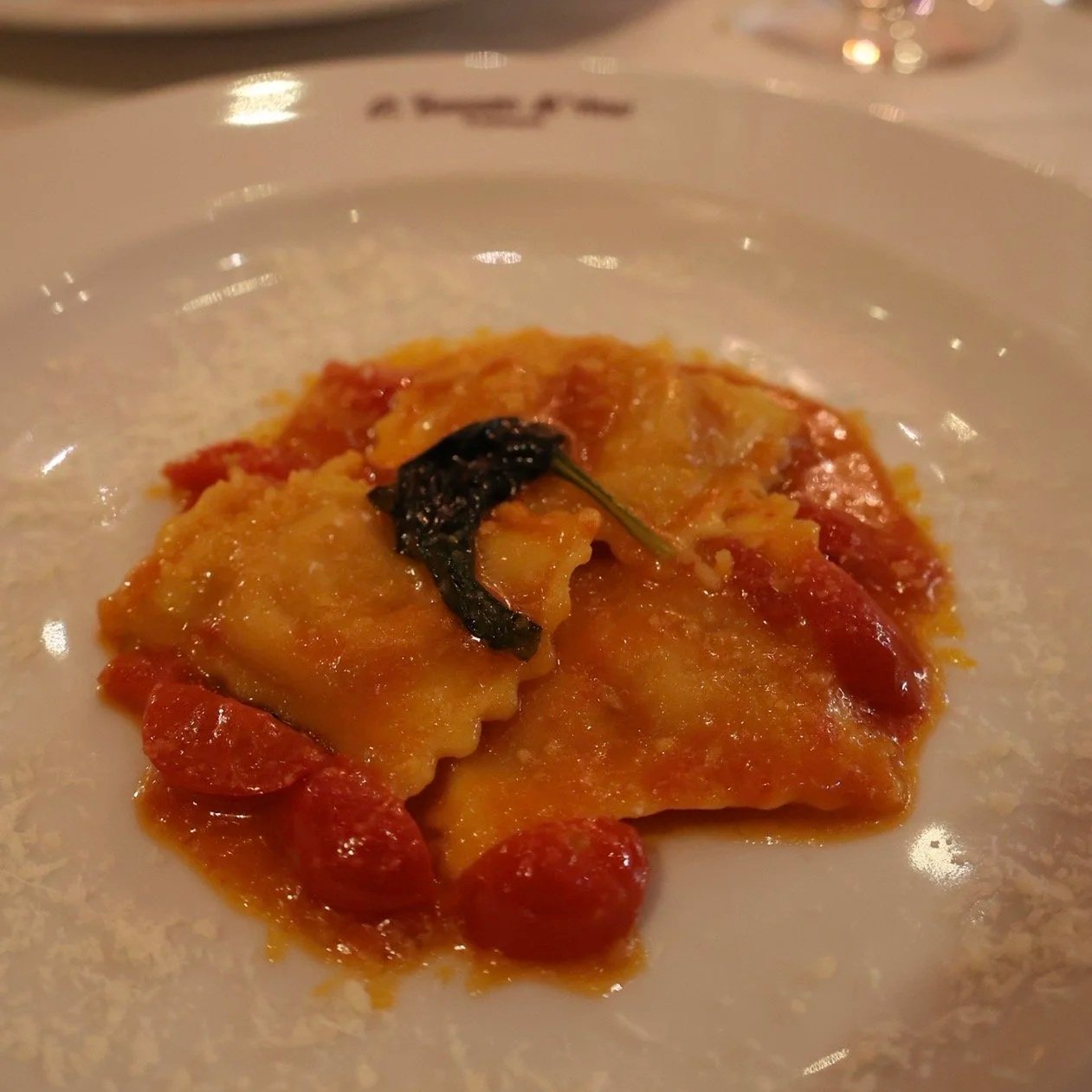 A plate of pasta with tomato sauce, cherry tomatoes, and a black garnish, served on a white dish.