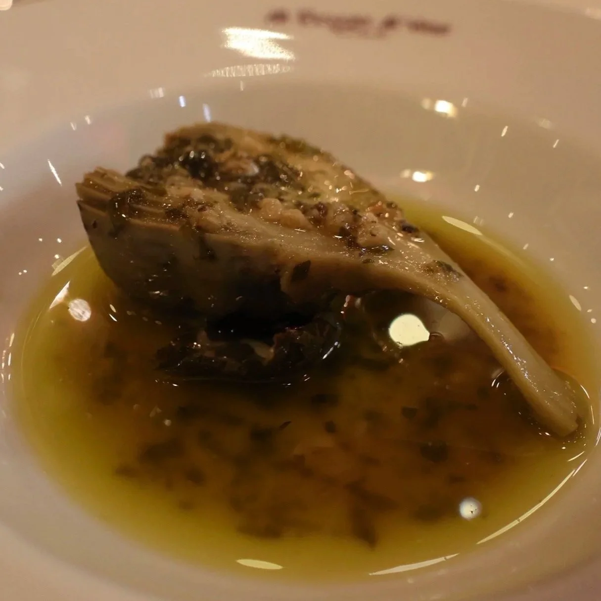 Close-up of a fish fillet in broth served in a white bowl on a dining table, with a bowl in the background.