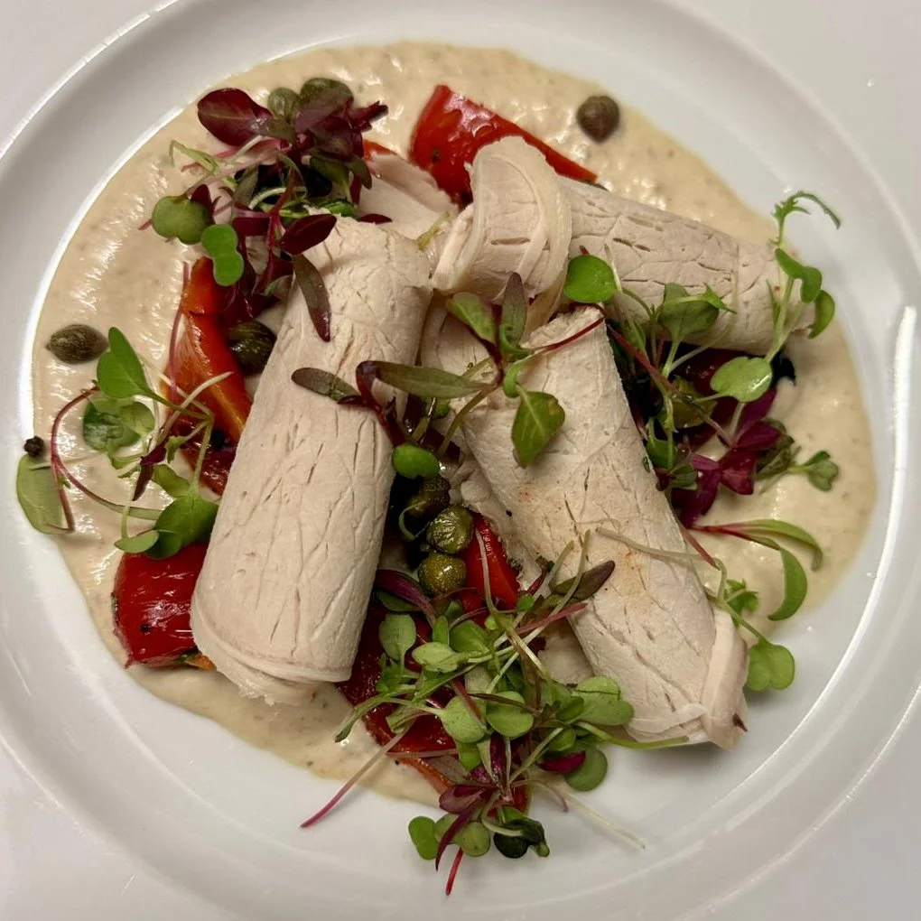 Cooked turkey breast slices with roasted red peppers, microgreens, and capers in a creamy sauce.