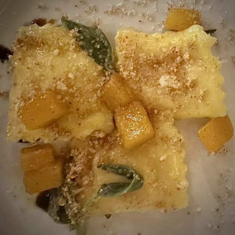 Close-up of a baked dish with chunks of yellow squash, grated cheese, and herbs in a creamy sauce.