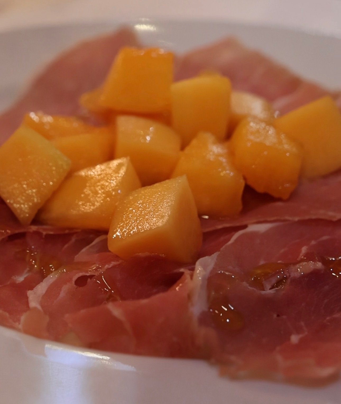 Sliced prosciutto with diced melon on a plate.