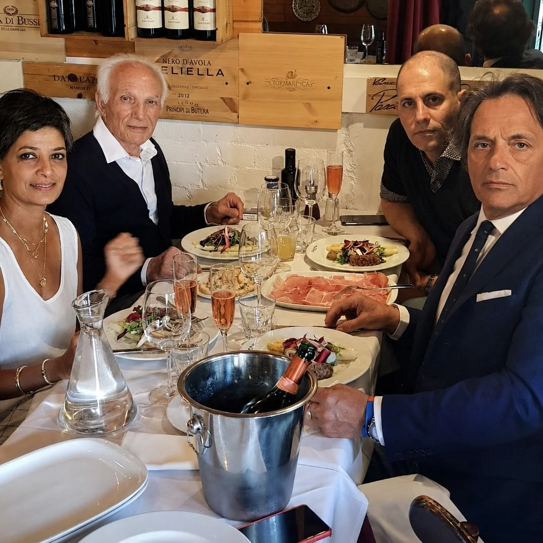 Group of five people sitting around a table with food and drinks in a restaurant, enjoying a meal together.