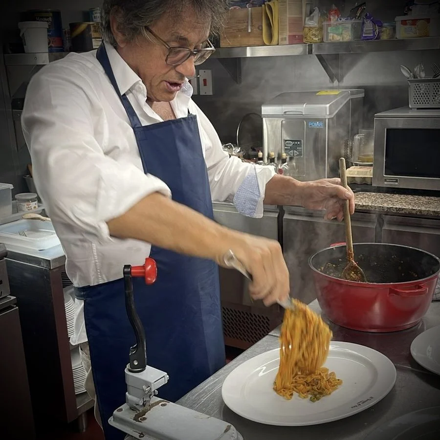 Person serving cooked pasta onto a white plate in a kitchen setting.