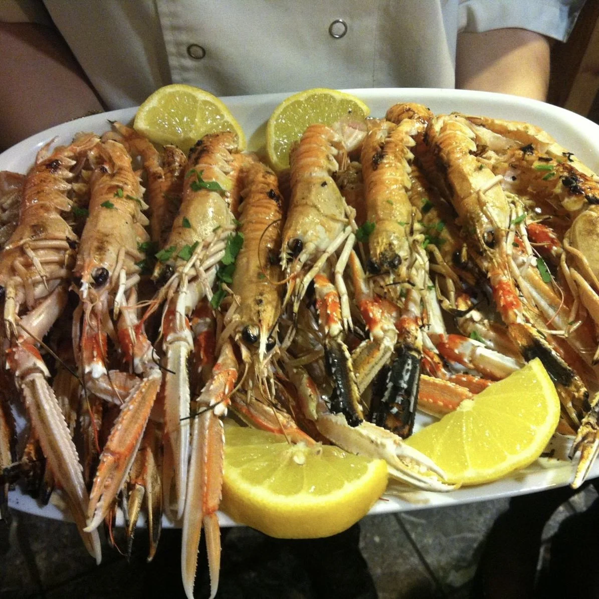 A tray of grilled lobster tails garnished with chopped parsley and lemon wedges.